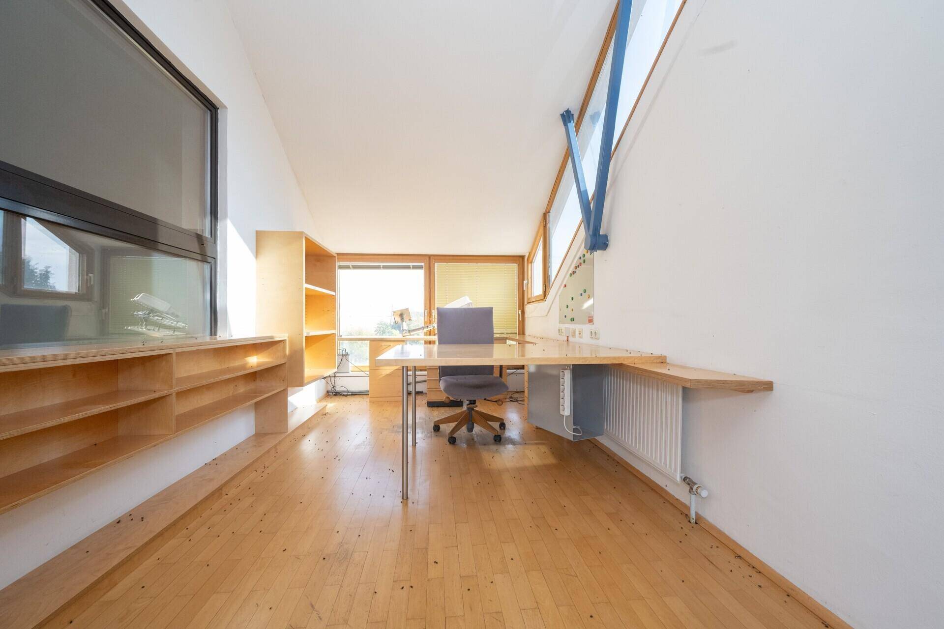 Langes Büro mit Holzparkett, durchgehender Arbeitsfläche und Regalen entlang der Wand.