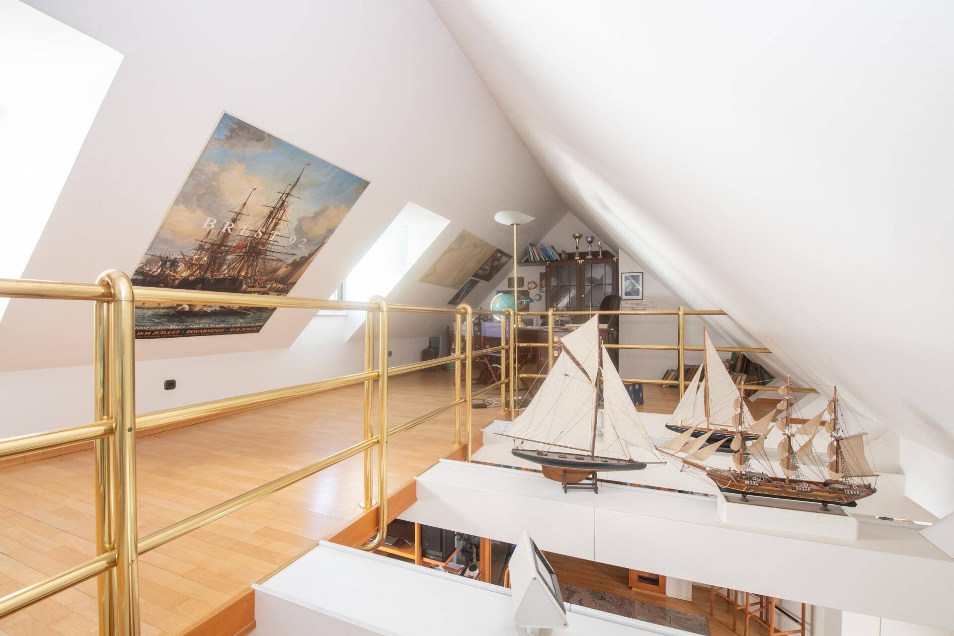 Helle Dachgeschossgalerie mit Schiffsmodellen, Holzfußboden und schrägen Wänden.