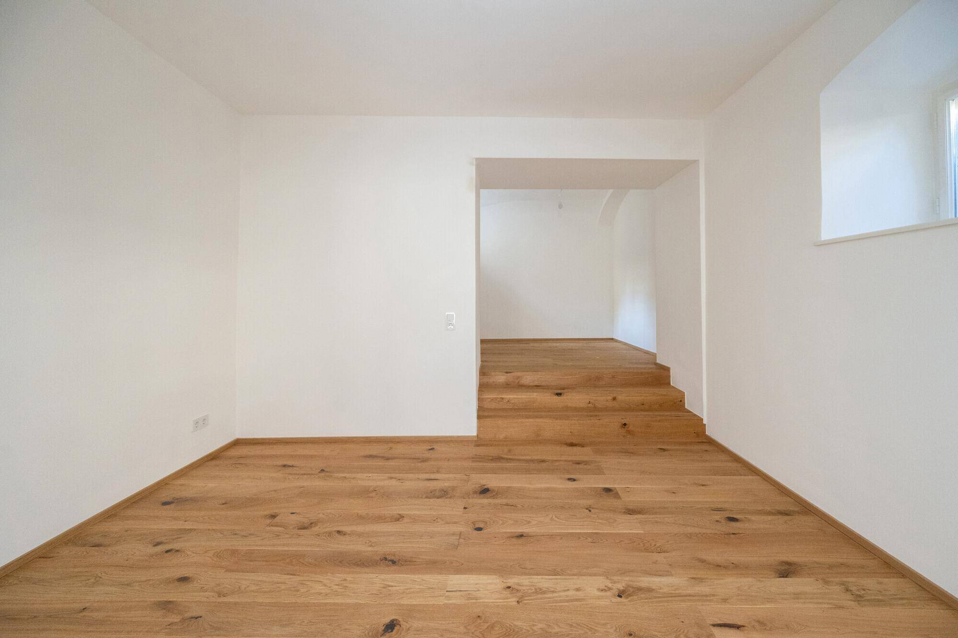 Heller Raum mit Holzboden und Treppe, die zu einem oberen Bereich führt.