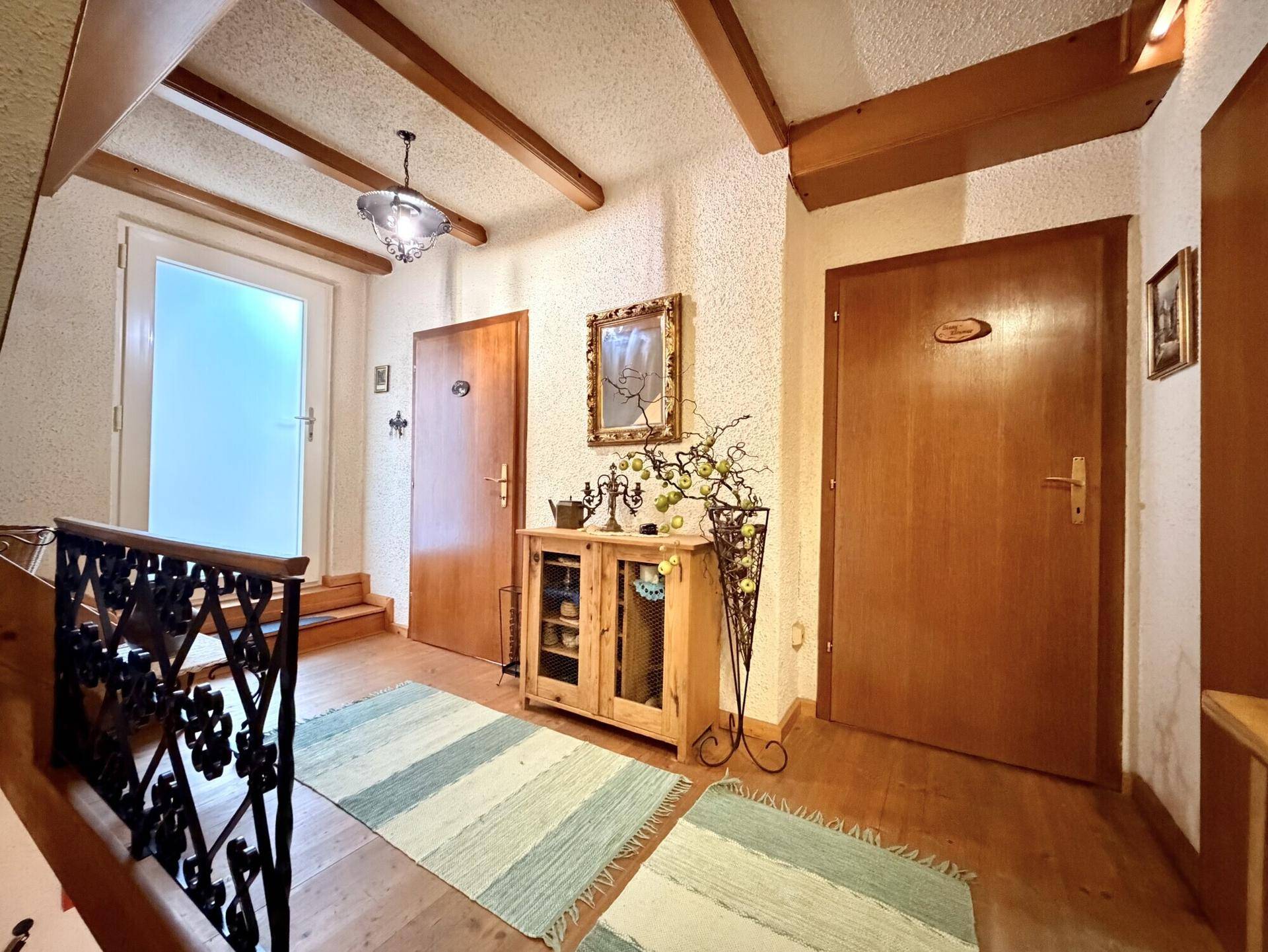 Heller Flur mit Holztreppe, rustikalem Geländer und Holzbalken an der Decke.