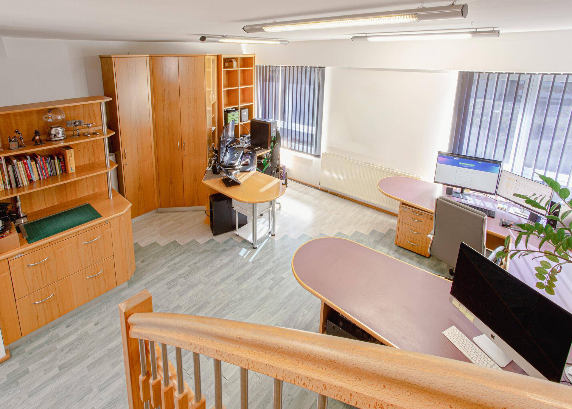 Geräumiges Büro mit mehreren Arbeitsplätzen, Holzmöbeln und großen Fenstern für viel Tageslicht.