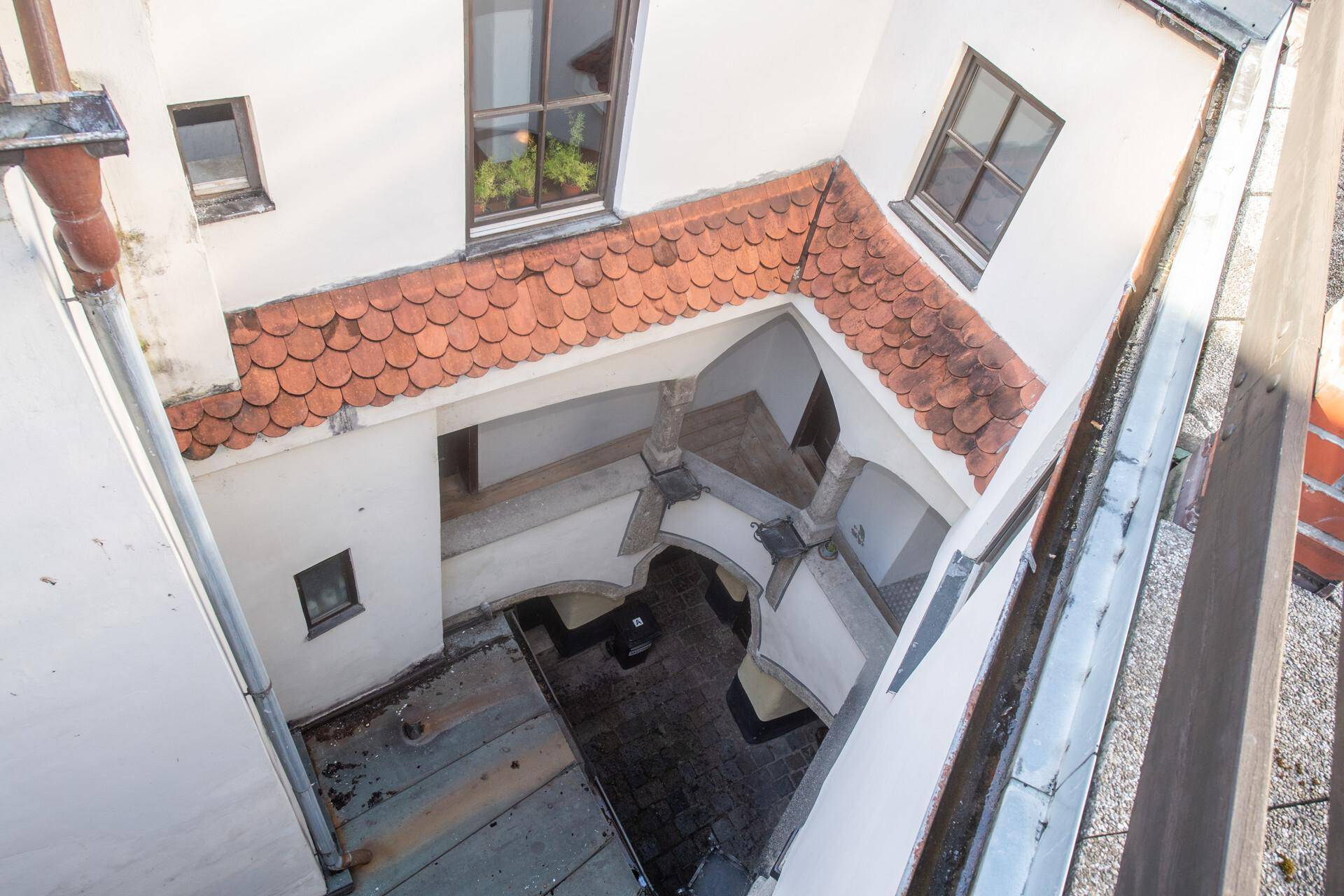 Blick von oben auf einen historischen Innenhof mit Ziegeldächern und weißen Fassaden.