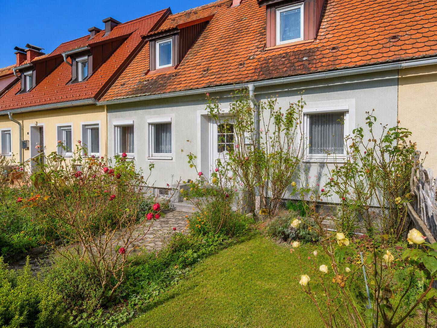 Vorderansicht eines Reihenhauses mit blühendem Vorgarten und gepflegtem Rasen.