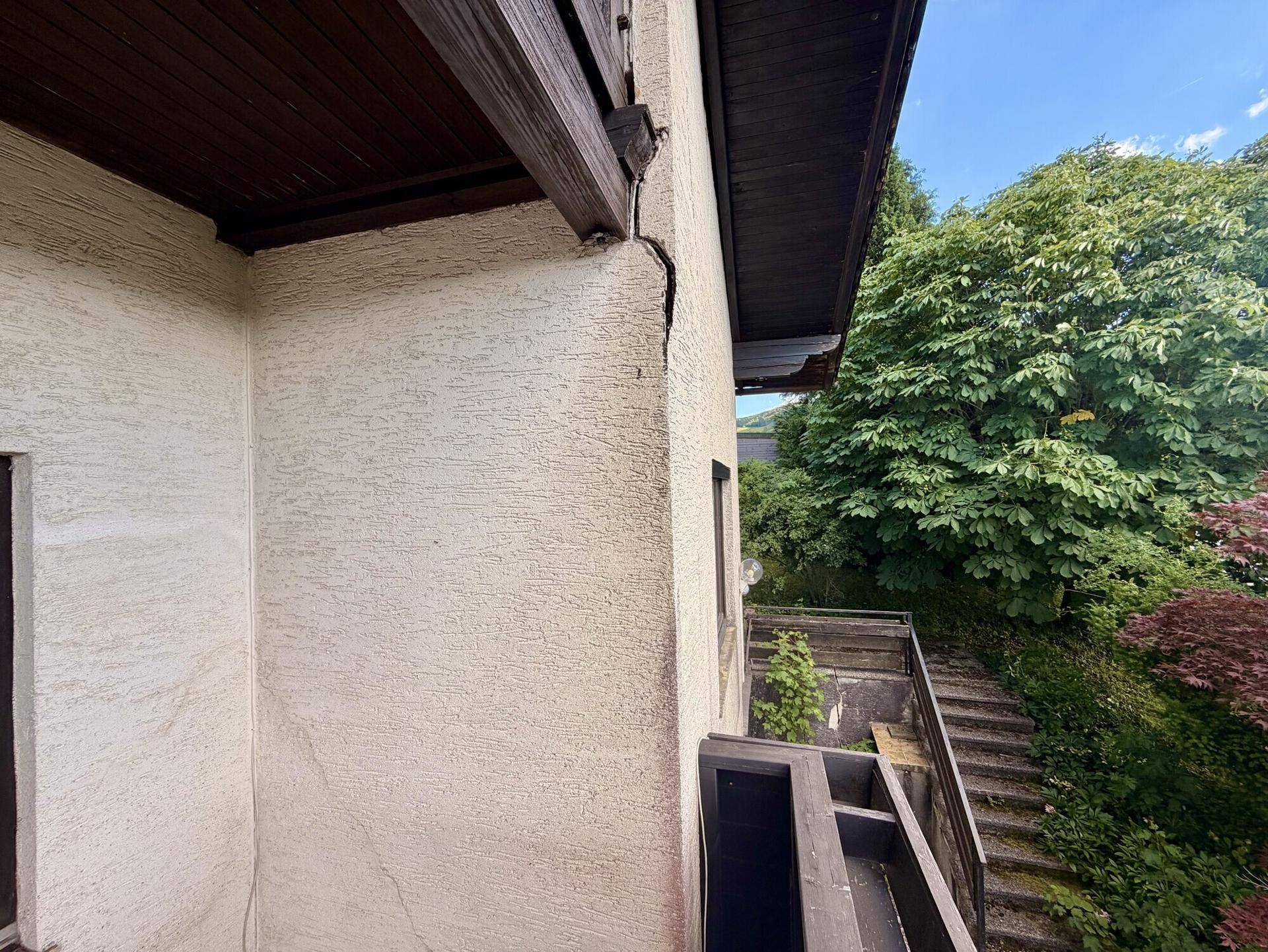 Blick vom Balkon auf die umliegende grüne Landschaft mit sichtbaren Rissen in der Fassade.