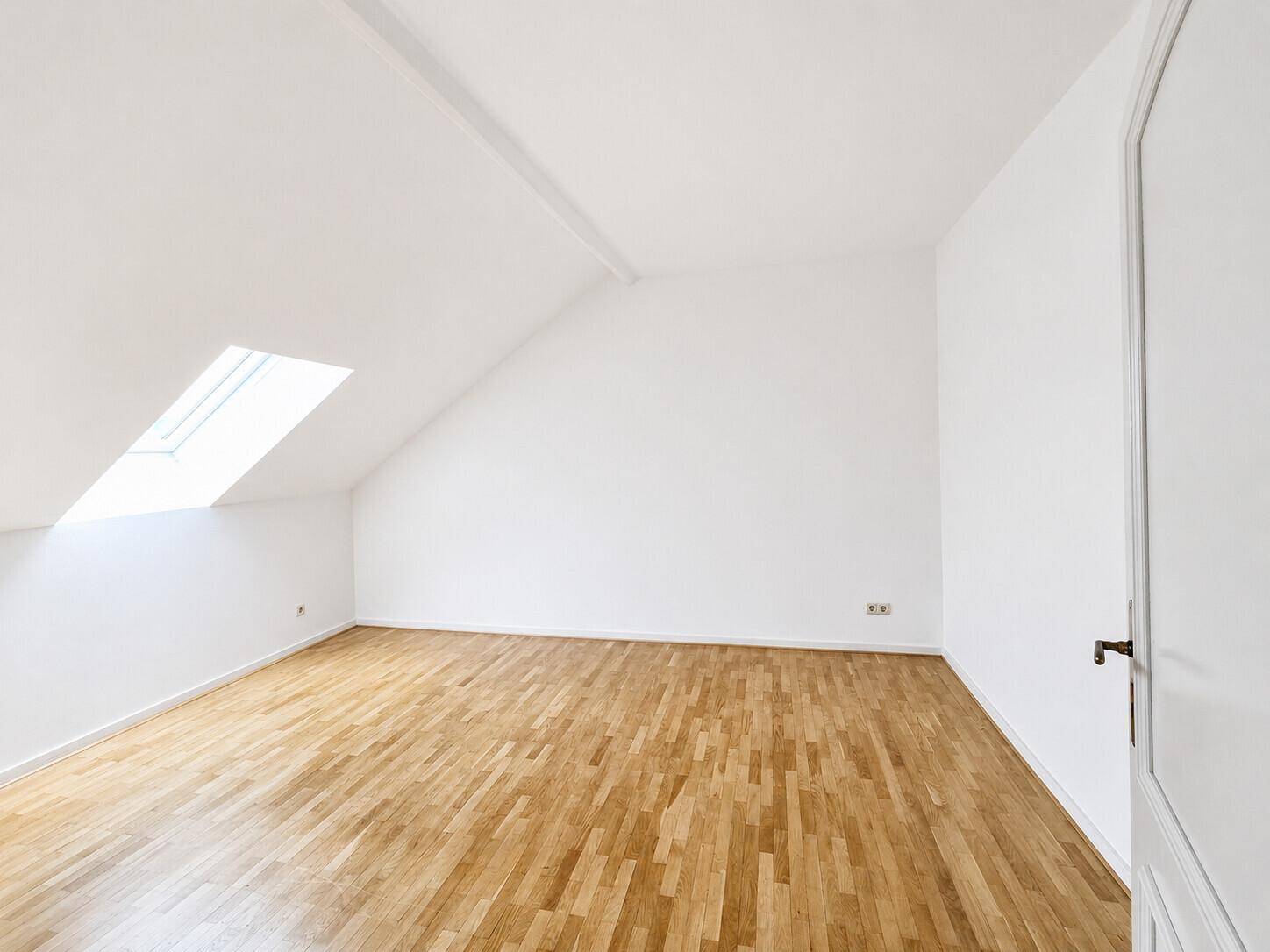 Leeres Zimmer im Dachgeschoss mit Holzboden und Dachfenster für viel Tageslicht.