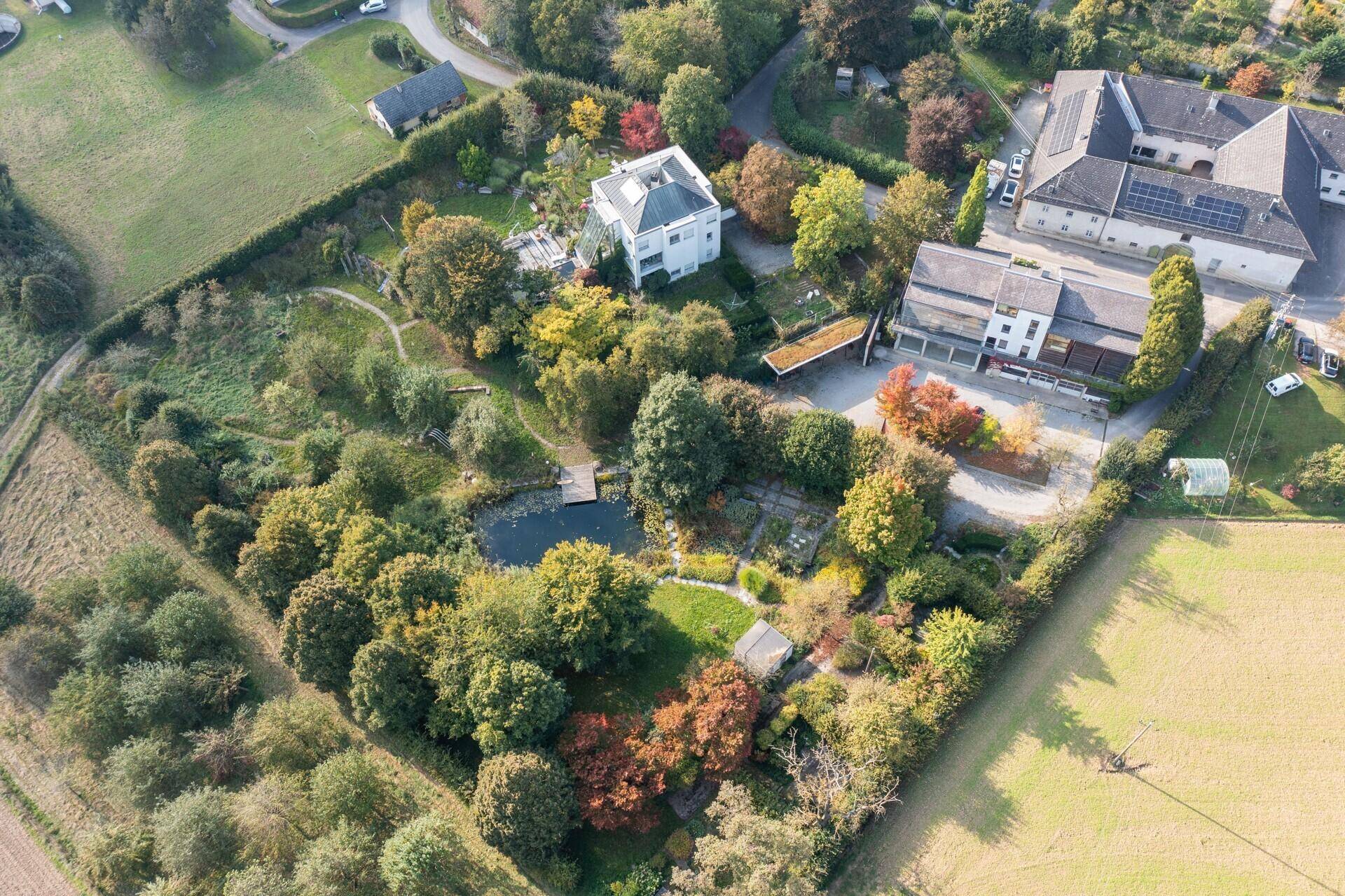 Weitläufige Luftaufnahme des Grundstücks mit großem Garten, Teich und umgebender Naturlandschaft.