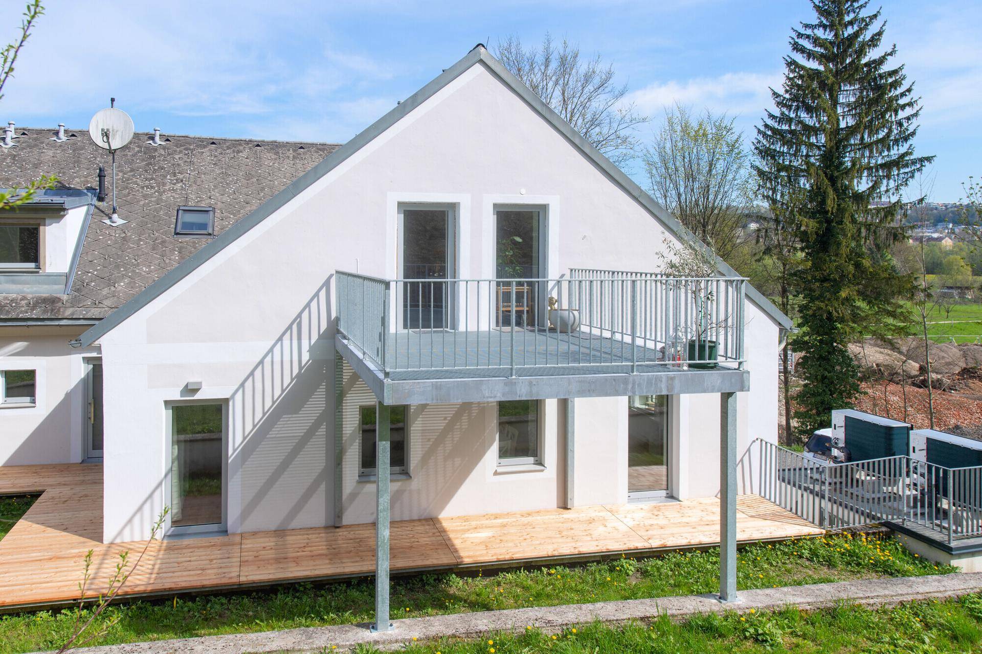 Nahaufnahme der modernen Hausfassade mit Balkon und Holzterrasse im Sonnenlicht.