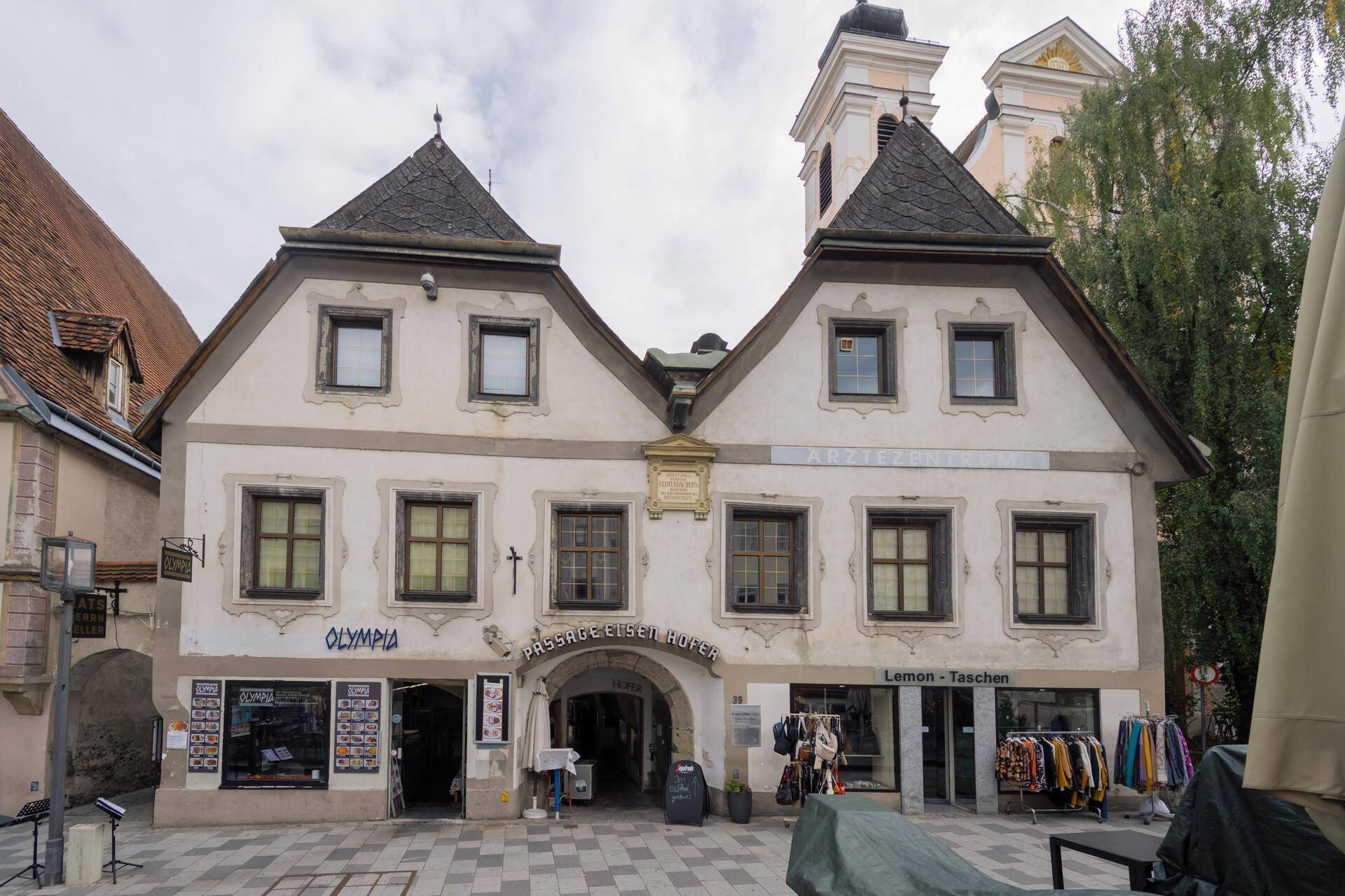 Historische Fassade mit zentralem Torbogen und Geschäften im Erdgeschoss, prägt das Stadtbild.
