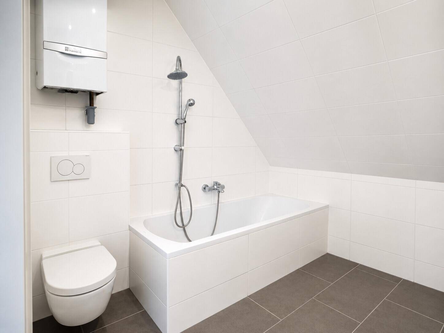 Modernes Badezimmer mit Badewanne, Dusche, Wand-WC und weißen Fliesen unter einer Dachschräge.