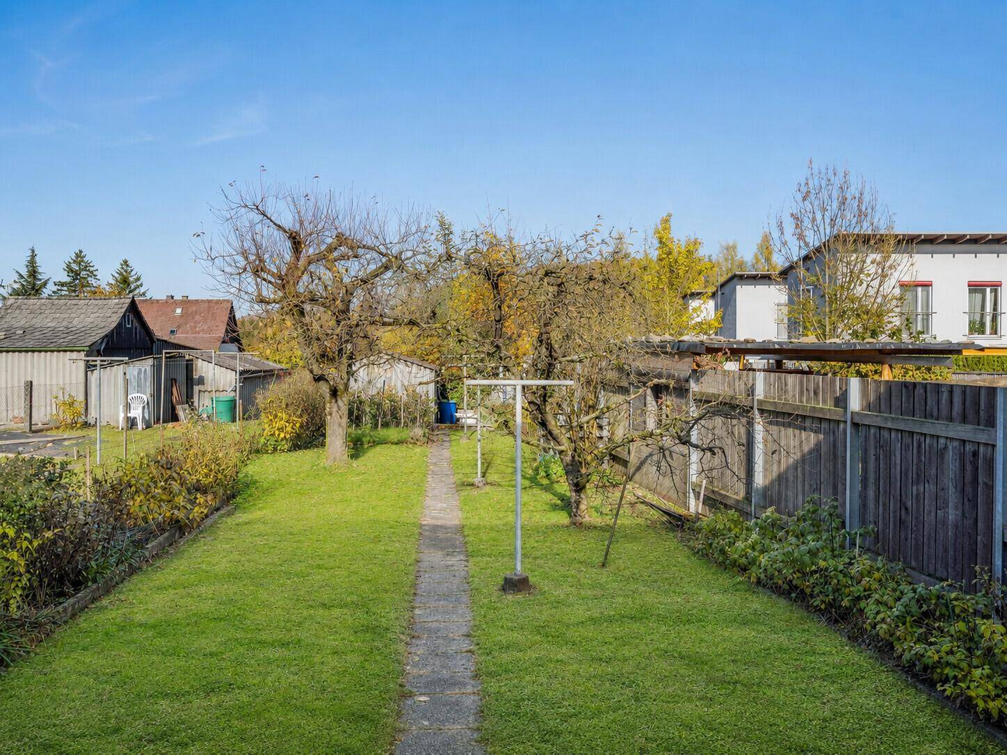 Langer, schmaler Garten mit Rasenweg, Obstbäumen und Holzzaun im hinteren Bereich.