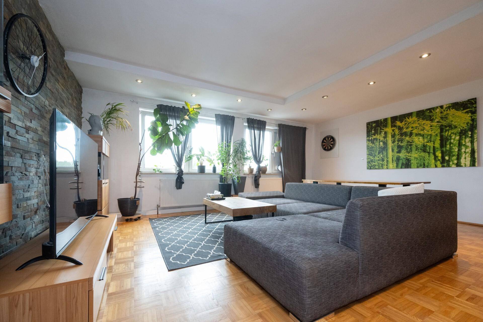 Großzügiges Wohnzimmer mit bequemer Sitzecke, Parkettboden und vielen Pflanzen.