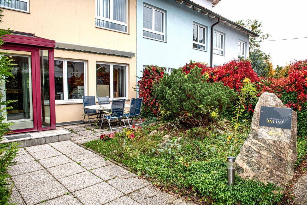 Gepflasterte Terrasse mit Gartenmöbeln und üppiger Bepflanzung vor dem Gebäude, ideal zum Entspannen.