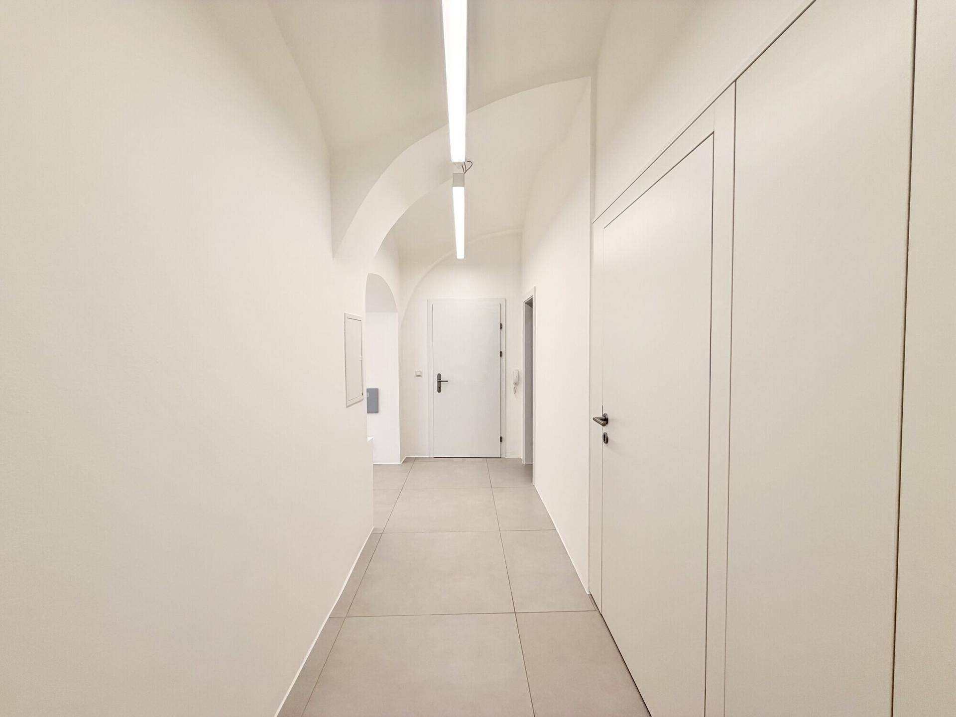 Langer, heller Flur mit modernen Lichtleisten und durchgehendem Fliesenboden.