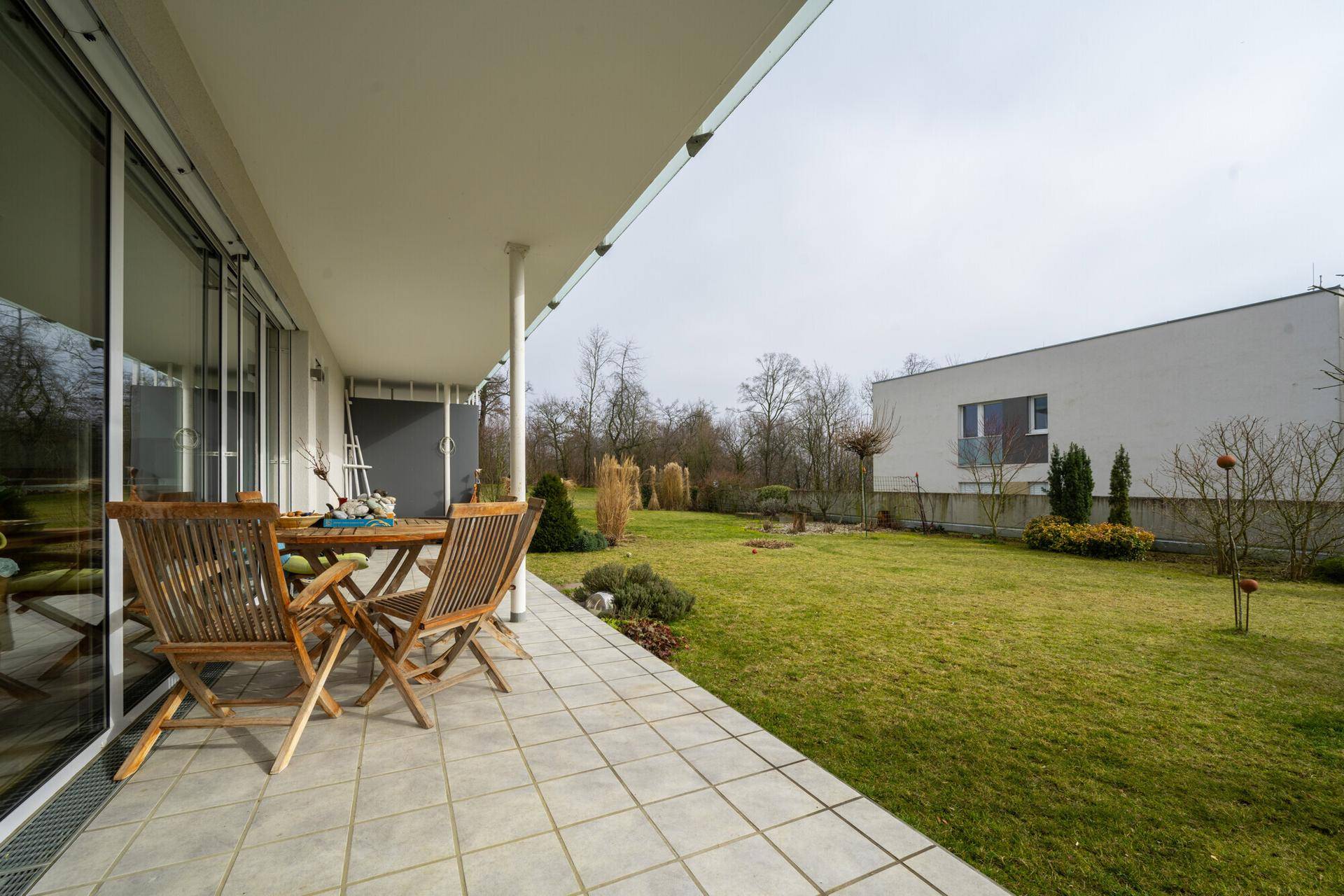 Überdachte Terrasse mit Gartenmöbeln und Blick auf die grüne Rasenfläche.