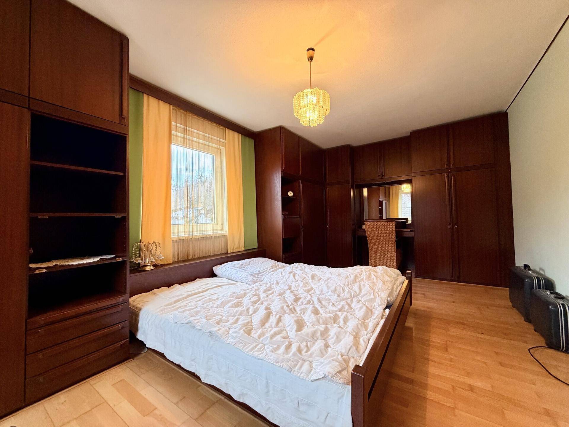 Schlafzimmer mit großem Doppelbett, dunklen Holzmöbeln und zwei Fenstern.