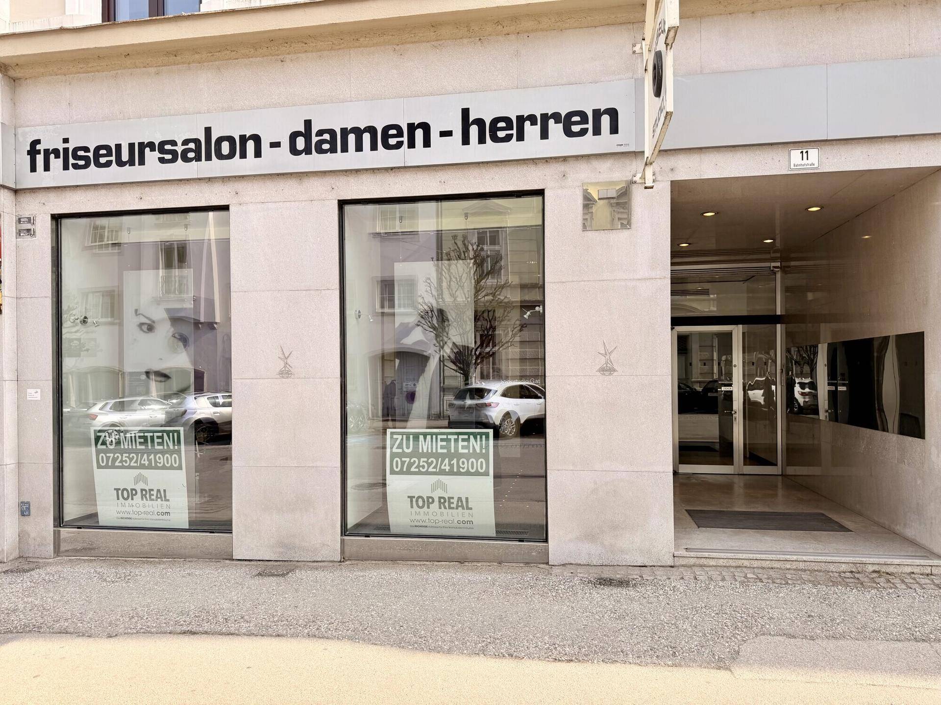 Außenansicht eines Friseursalons mit großen Schaufenstern und Werbeschildern.