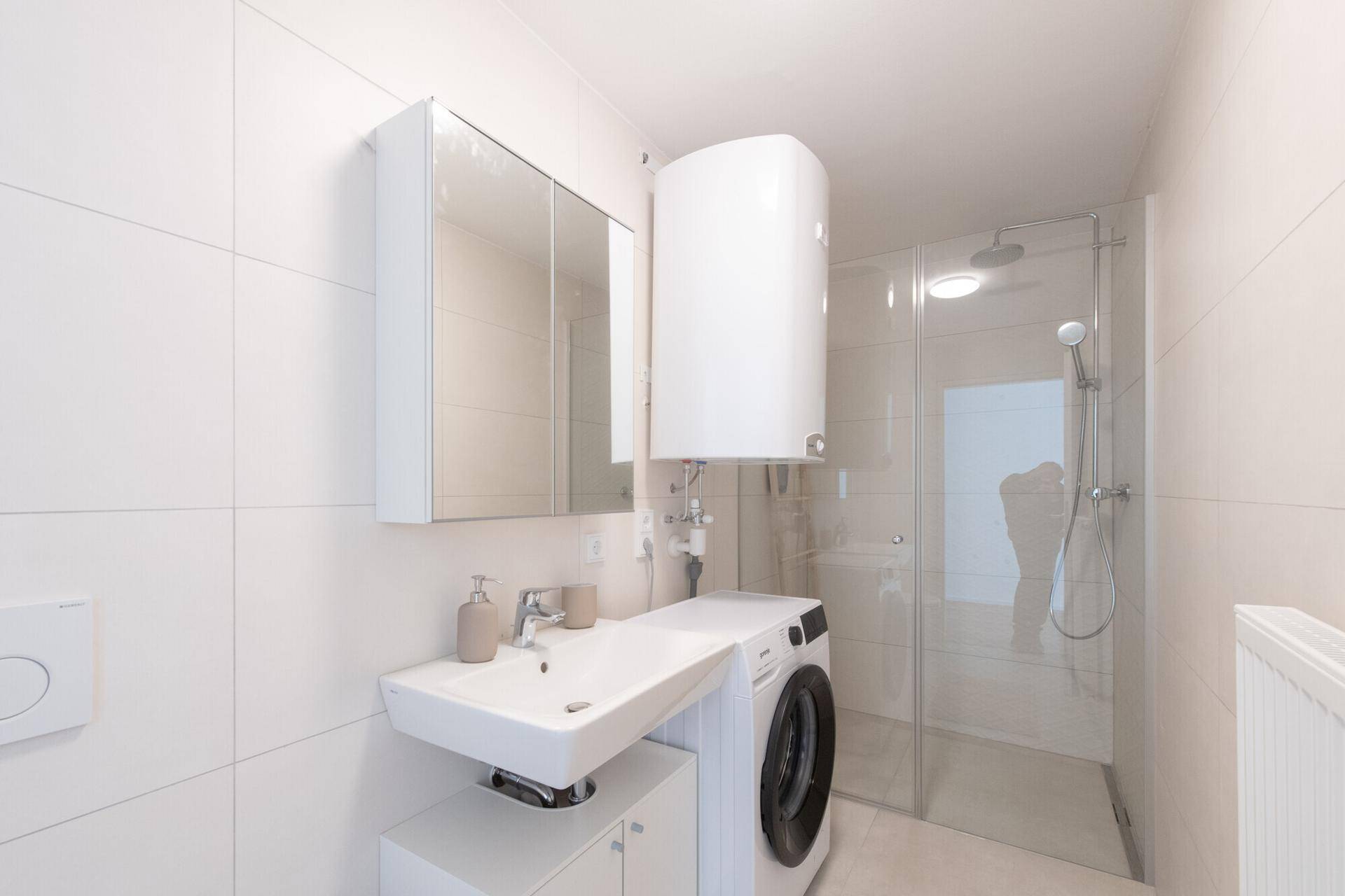 Modernes Badezimmer mit Dusche, Waschbecken, Spiegelschrank und Waschmaschine.