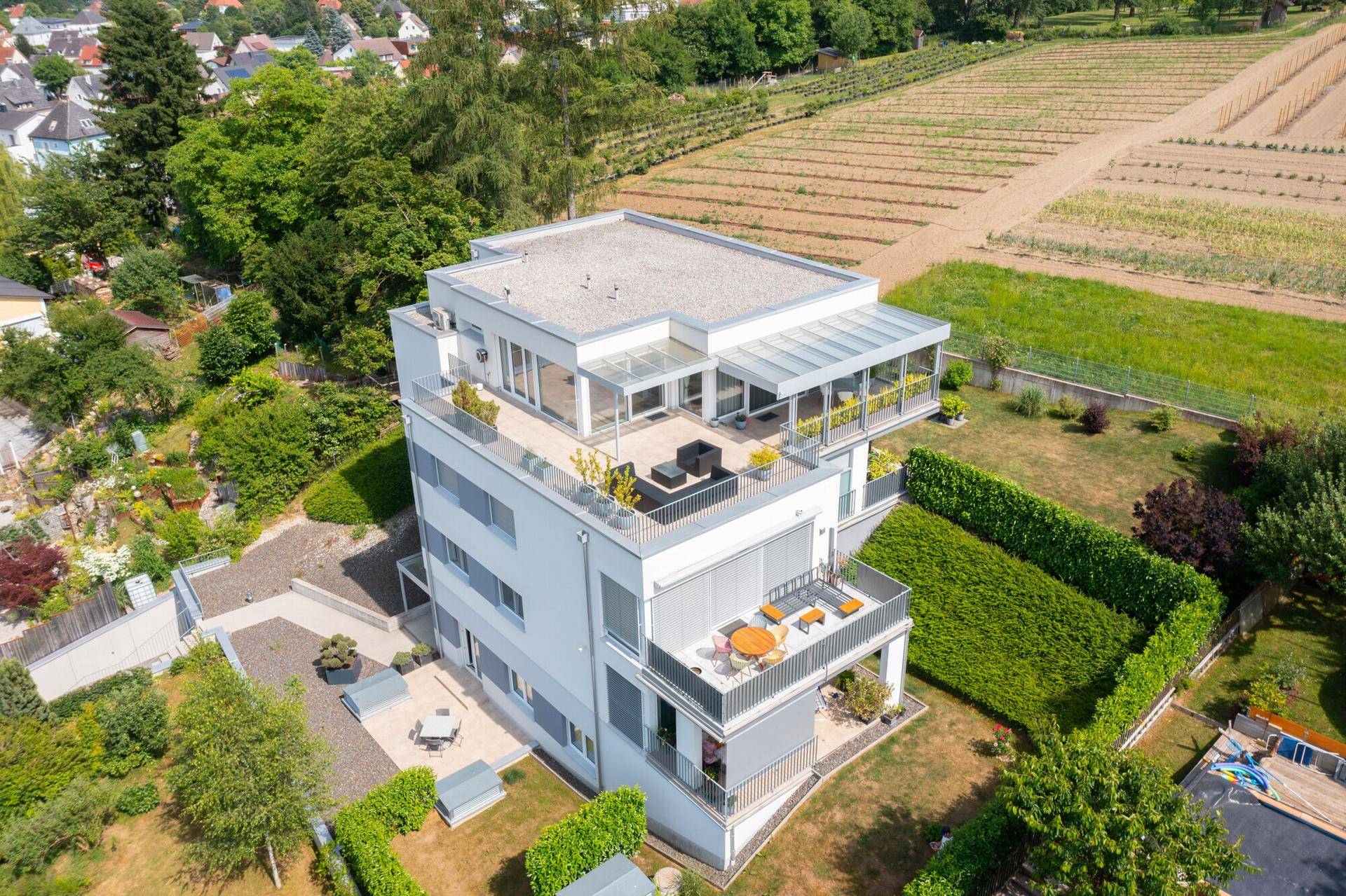 Modernes Mehrfamilienhaus mit Flachdach und mehreren Terrassen in grüner Umgebung.