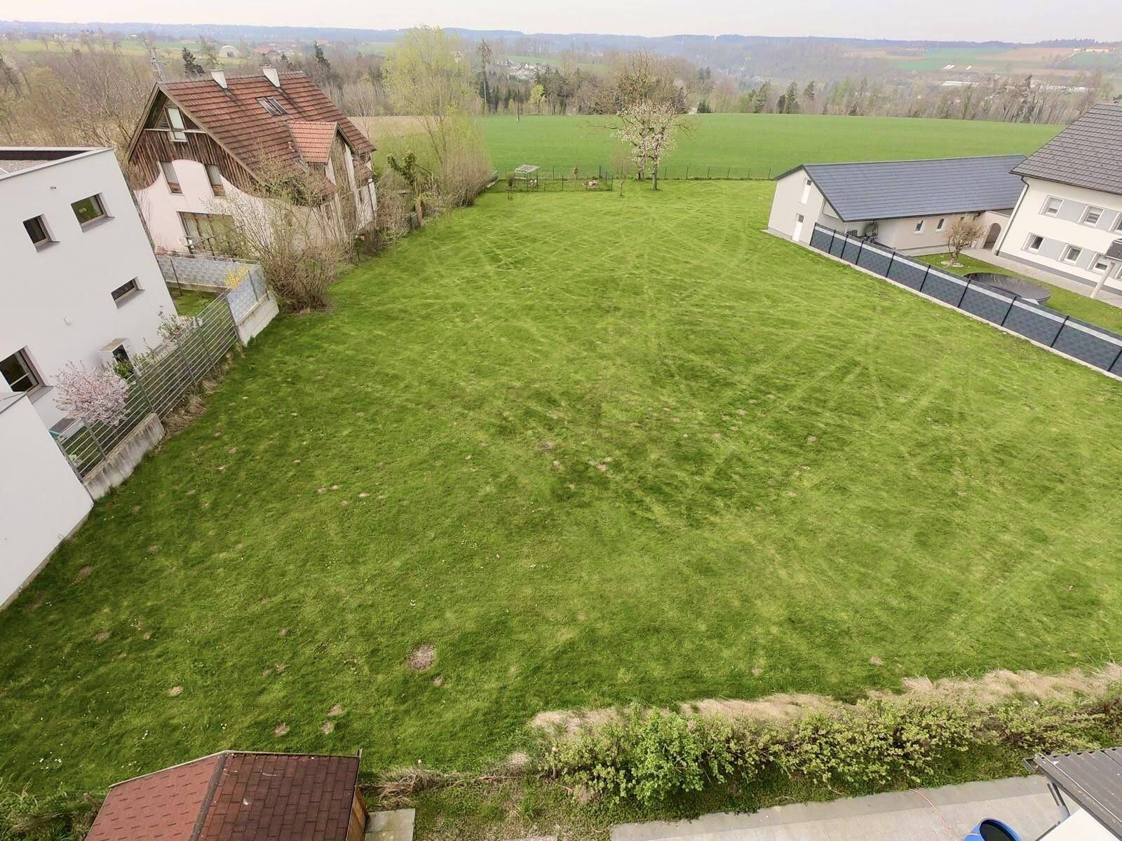 Vogelperspektive auf ein großes, grünes Grundstück umgeben von Wohnhäusern und Natur.