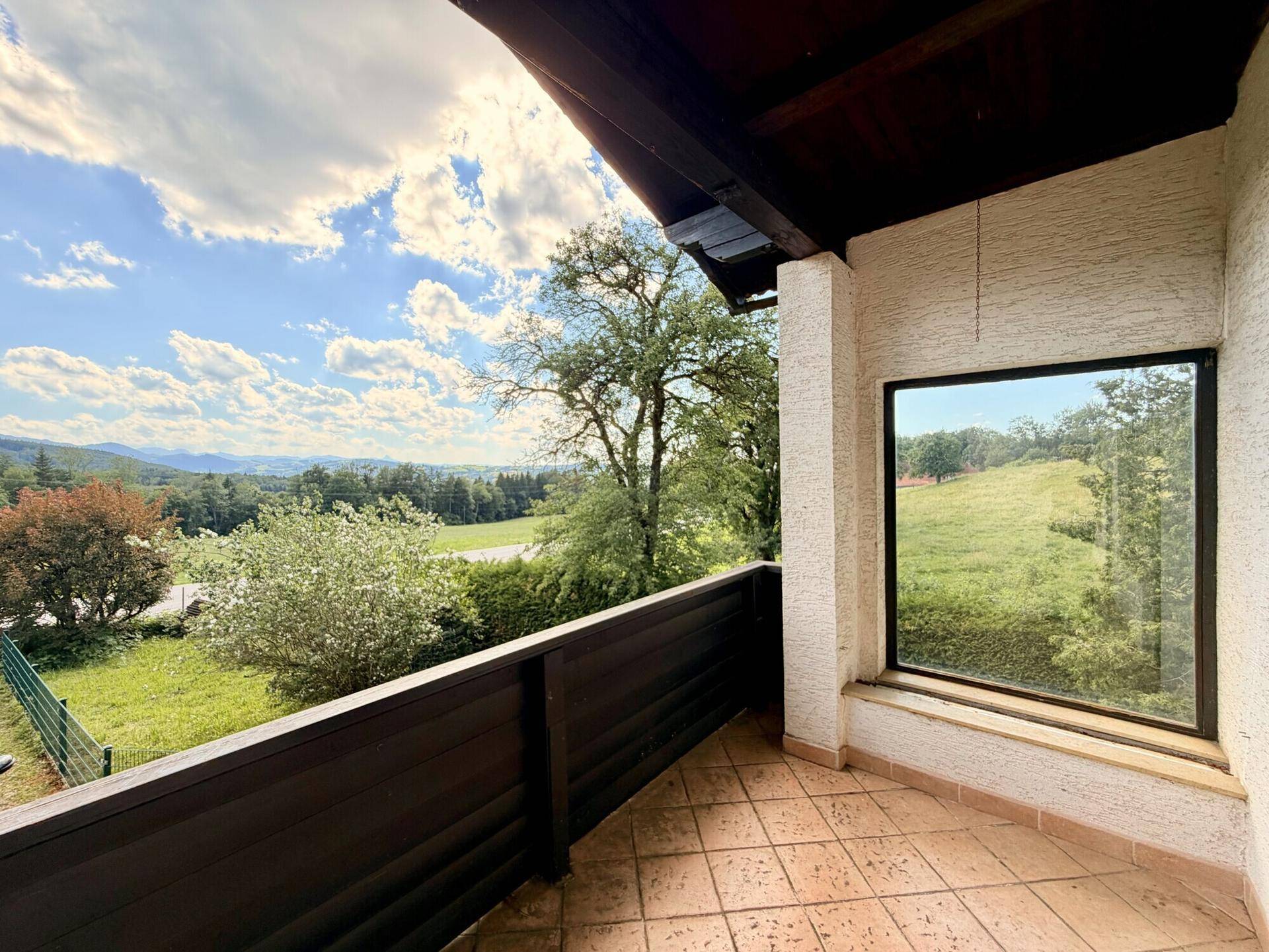 Geräumiger Balkon mit Fliesenboden und weitem Blick über die grüne Landschaft.