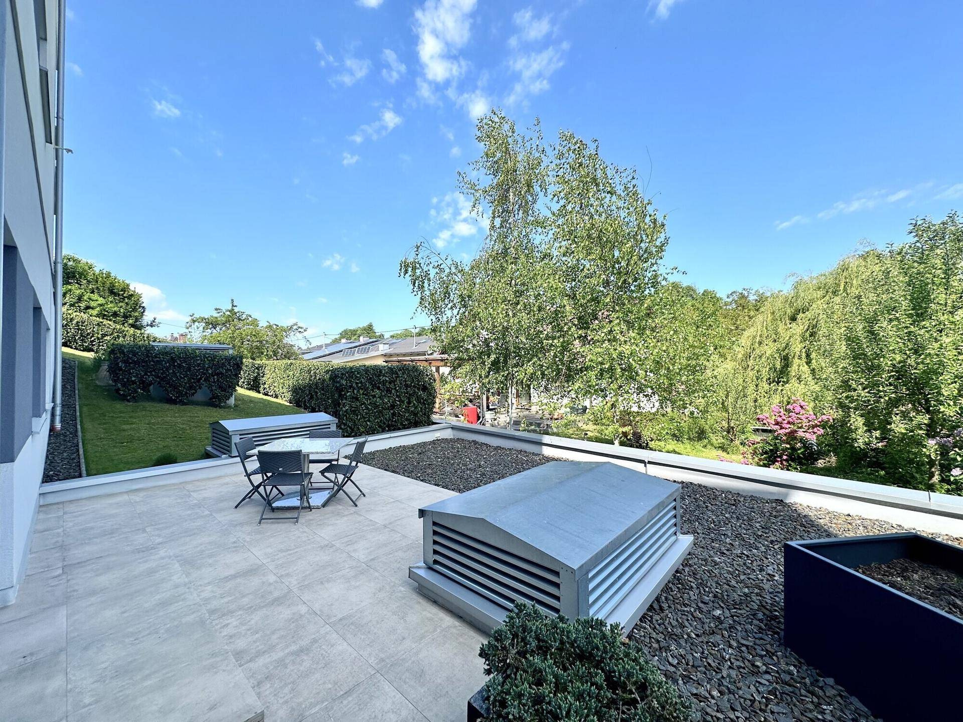 Große Dachterrasse mit Sitzgelegenheiten und Blick ins Grüne unter blauem Himmel.