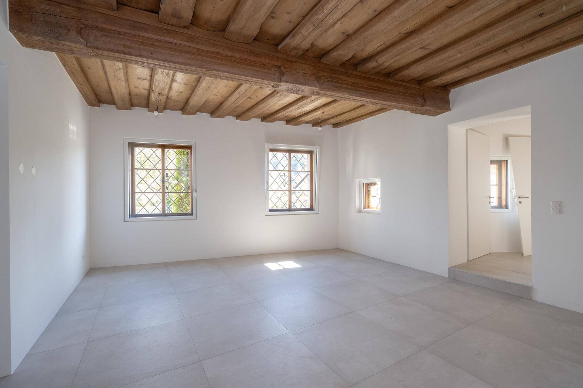 Großer, heller Raum mit rustikaler Holzbalkendecke und Fliesenboden, ideal als Wohnbereich.
