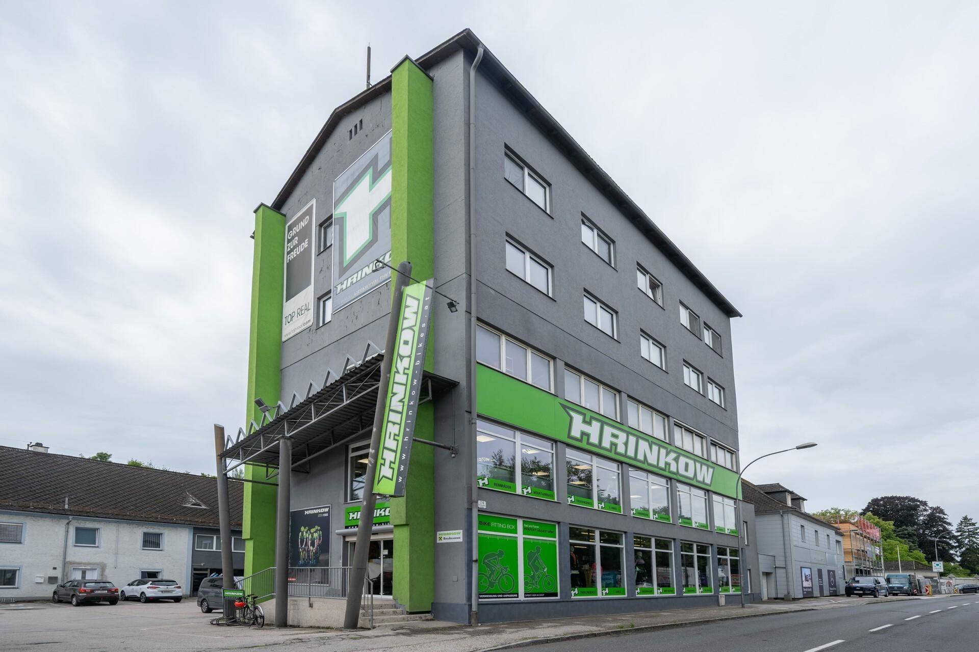 Modernes Geschäftsgebäude mit grauer Fassade und auffälligen grünen Akzenten an der Straße.
