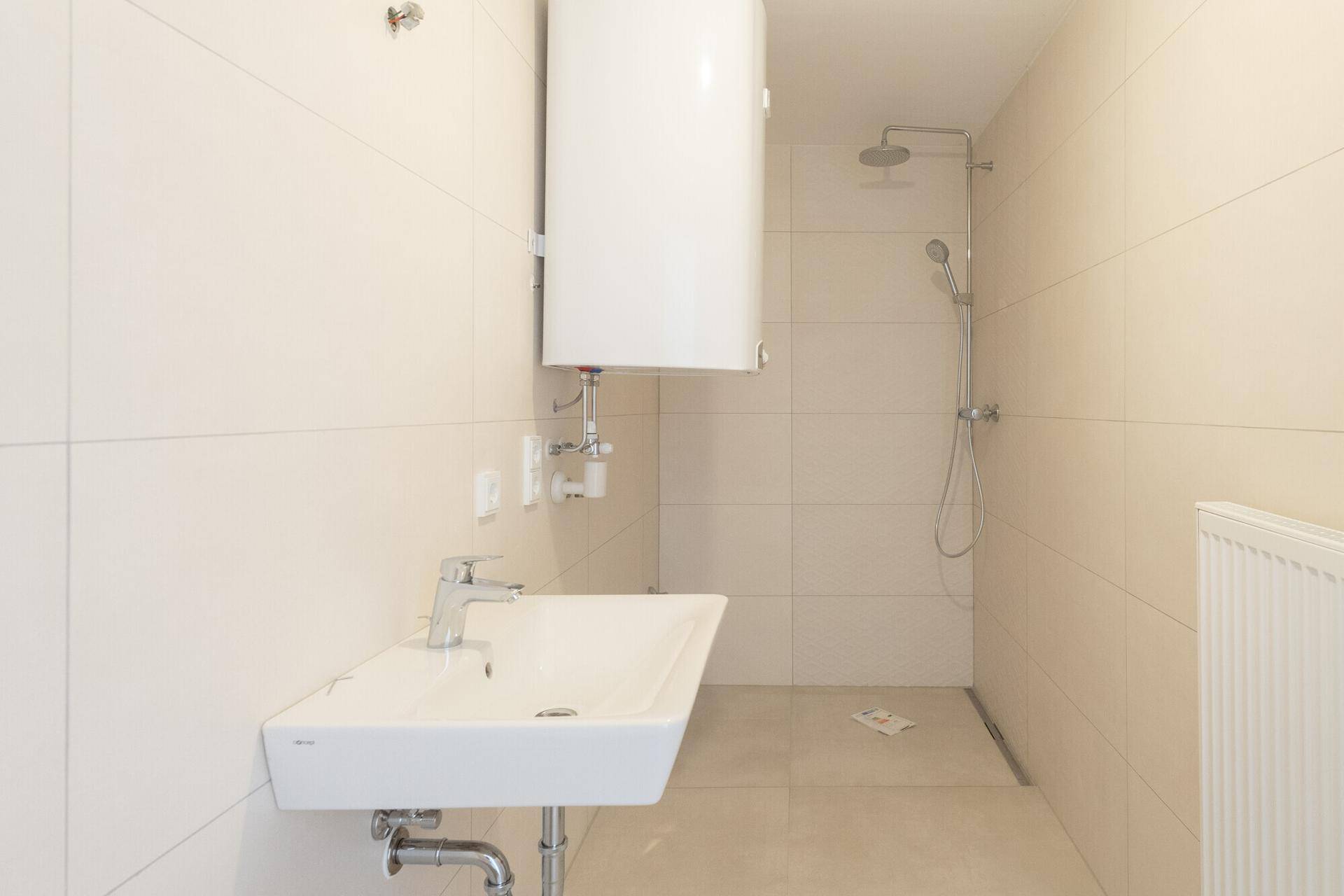 Modernes Badezimmer mit ebenerdiger Dusche, Waschbecken und Boiler in hellen Fliesen.