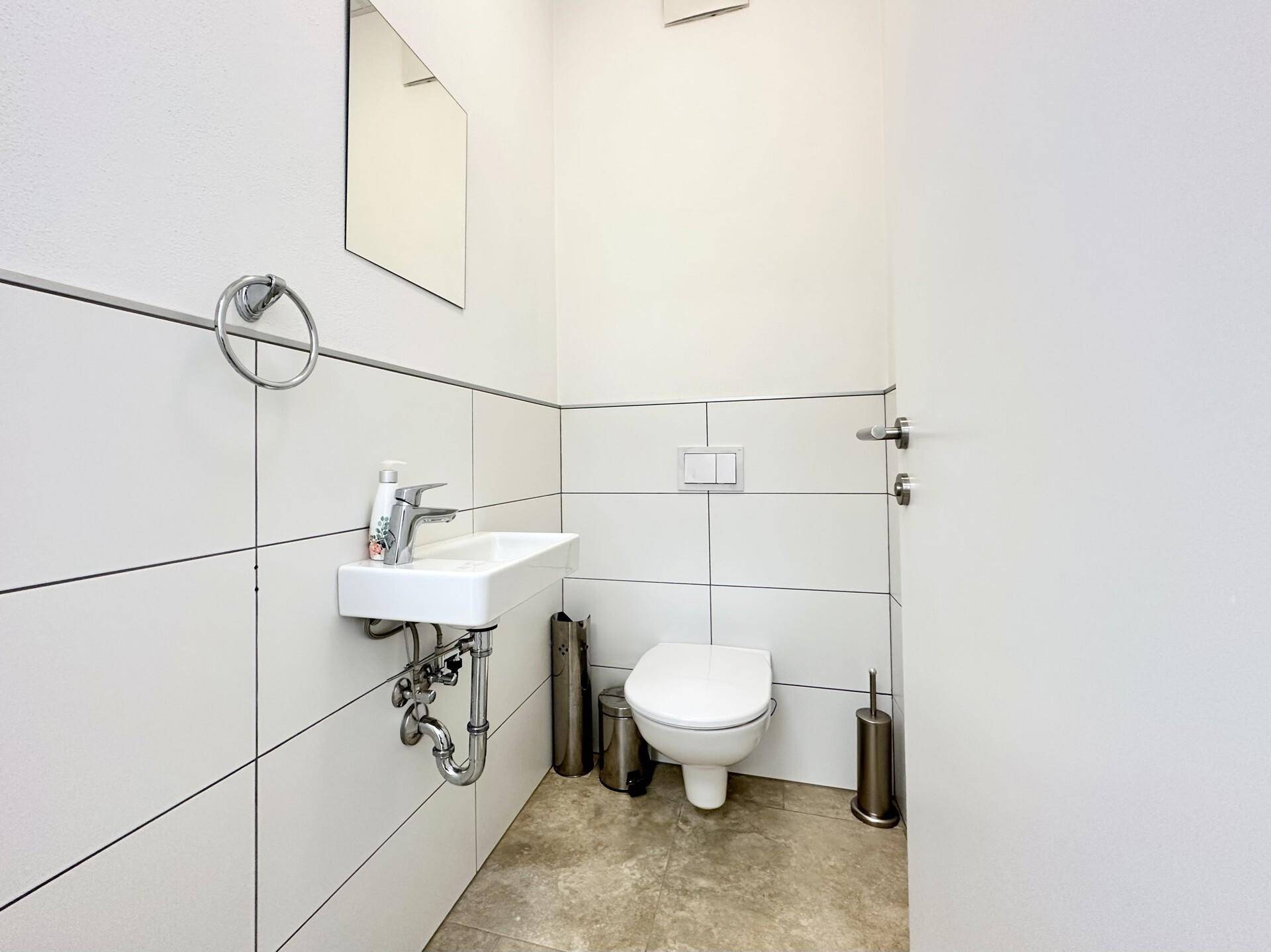 Kleines Gäste-WC mit wandhängender Toilette, kleinem Waschbecken und weißen Fliesen an den Wänden.