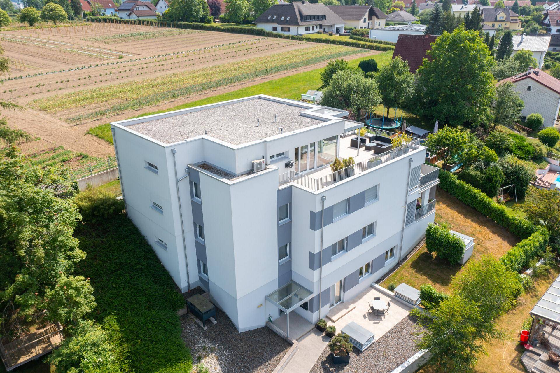 Luftaufnahme eines modernen Wohngebäudes mit Flachdach und angrenzenden Feldern.