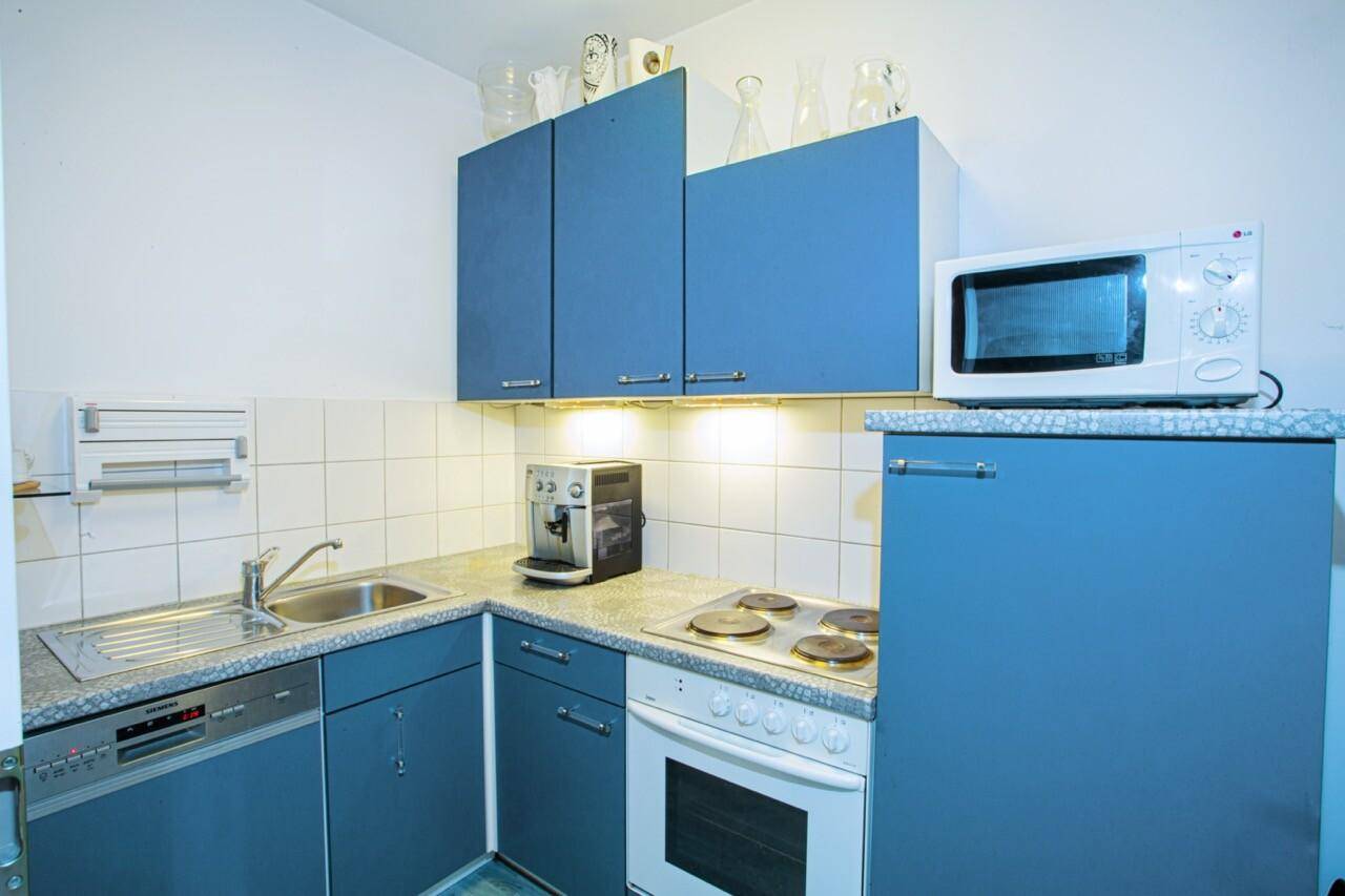 Funktionale Küche mit blauen Schränken, Spülmaschine, Mikrowelle und Kaffeemaschine.