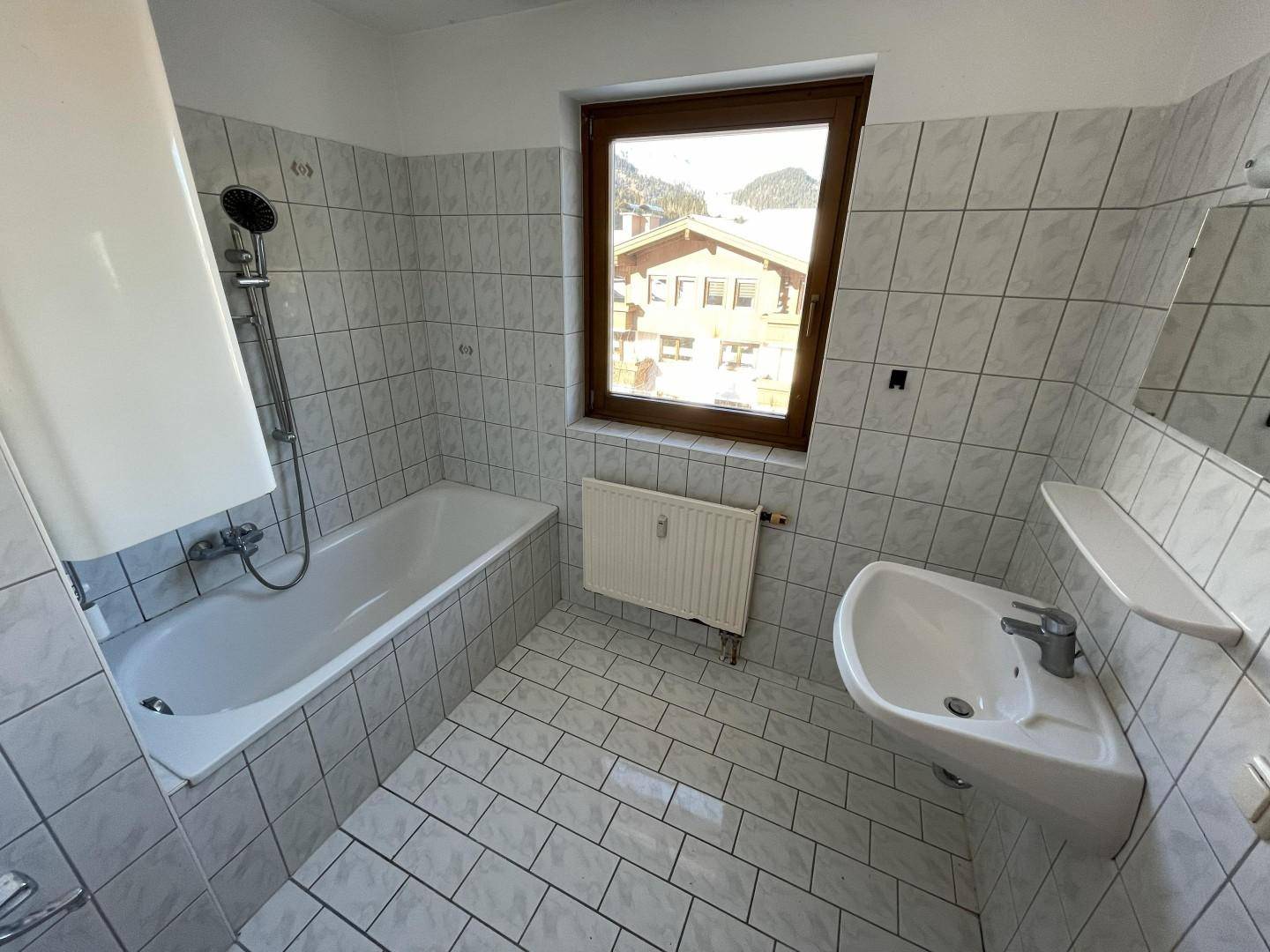 Gefliestes Badezimmer mit Badewanne, Waschbecken und Fenster, in einem gepflegten Zustand.
