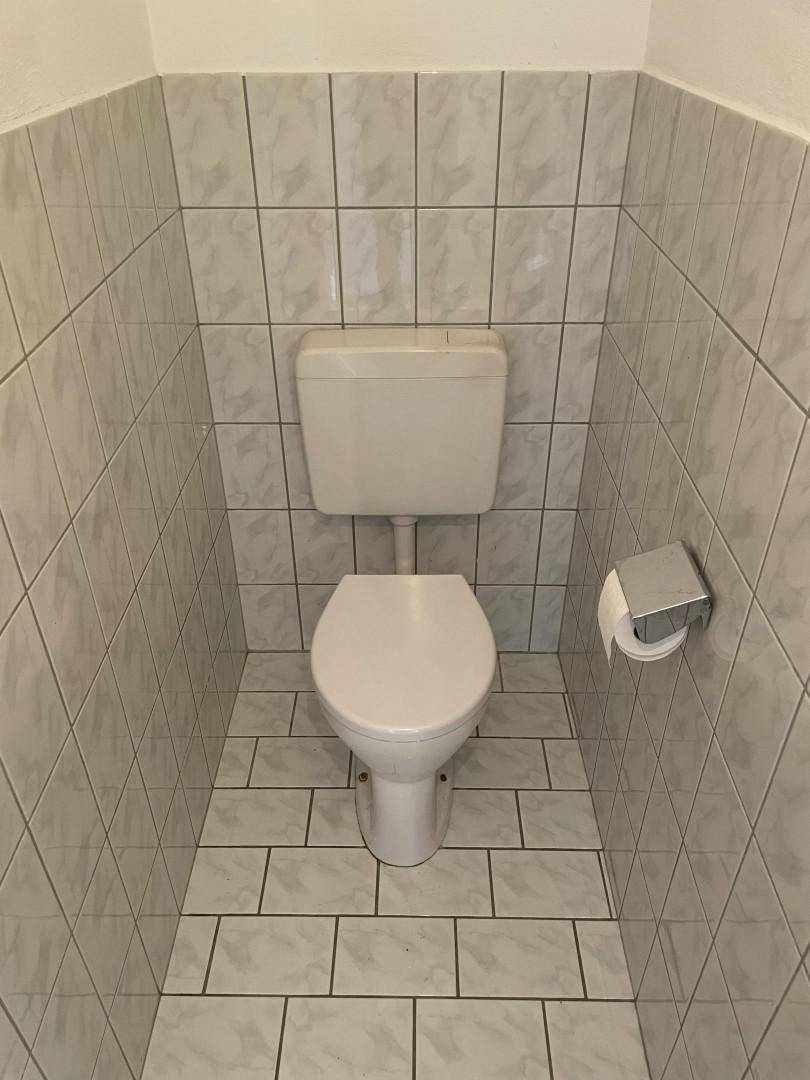 Separates WC mit hellen Fliesen an Wänden und Boden, funktional und sauber.