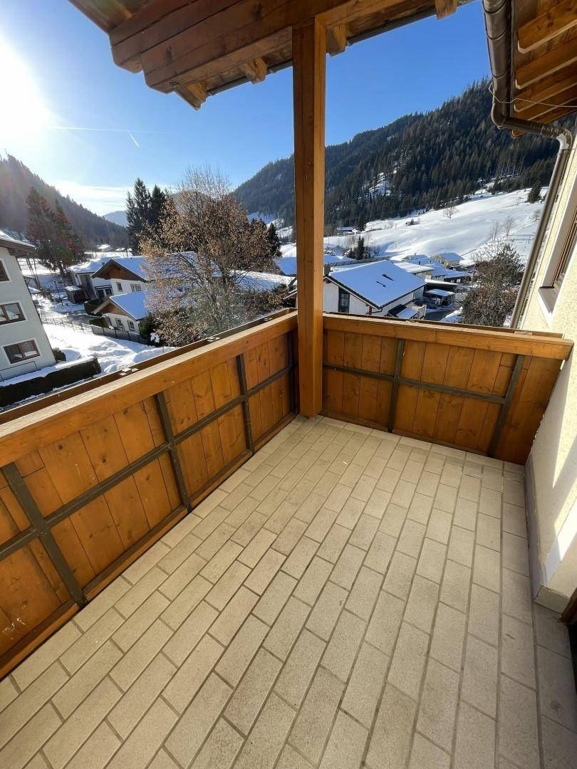 Sonnenverwöhnter Balkon mit Fliesenboden und Holzbrüstung, bietet einen weiten Blick auf die verschneiten Berge.