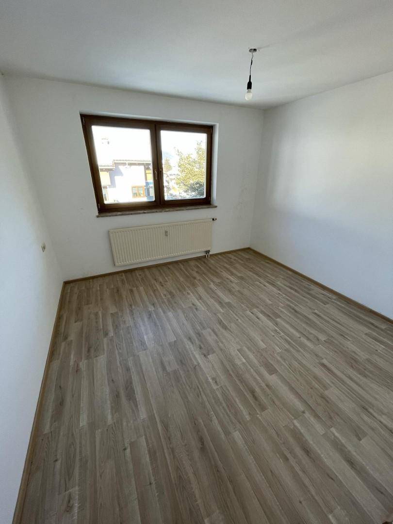 Leeres Schlafzimmer mit Laminatboden, Fenster und Heizkörper, ideal für persönliche Einrichtung.