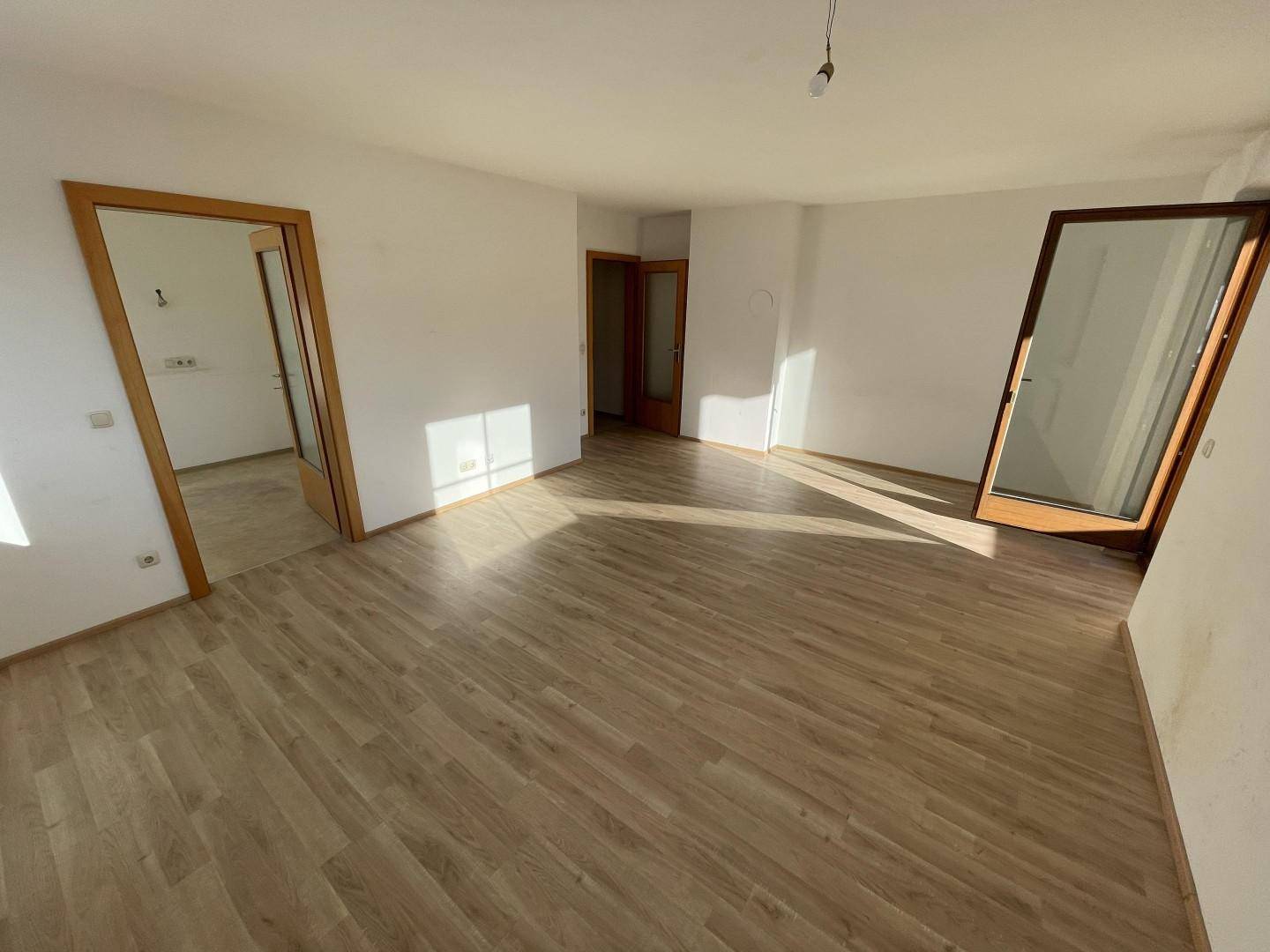 Helles, leeres Zimmer mit Laminatboden und mehreren Türen, bereit zur individuellen Gestaltung.