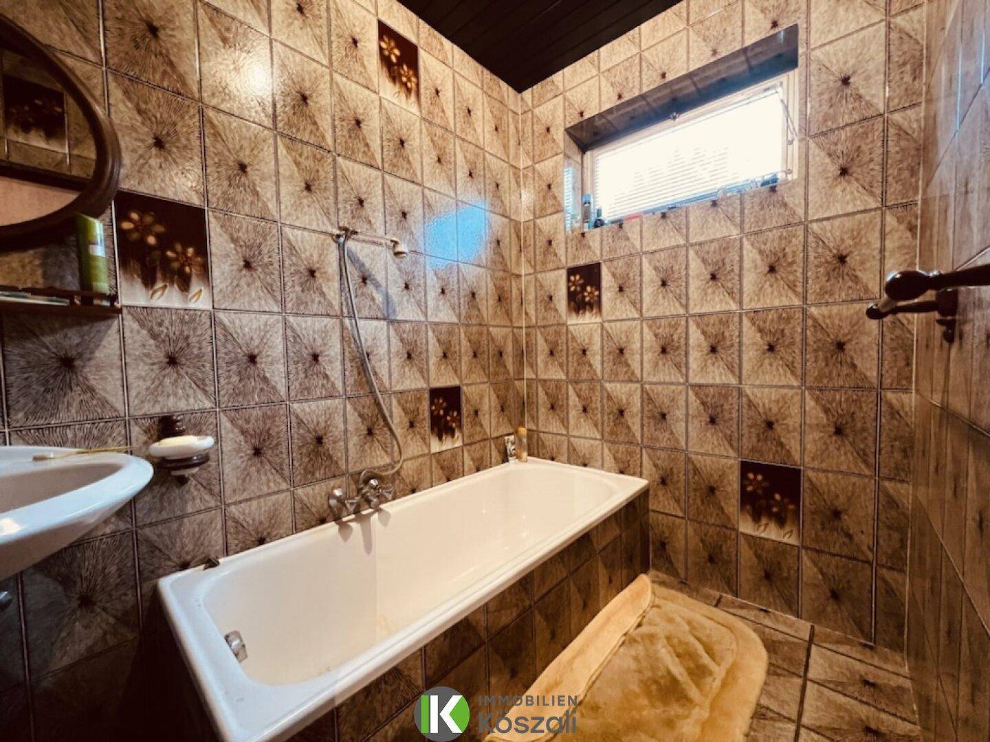 Badezimmer mit braunen Fliesen, Badewanne und kleinem Fenster, typisch für die 80er Jahre.