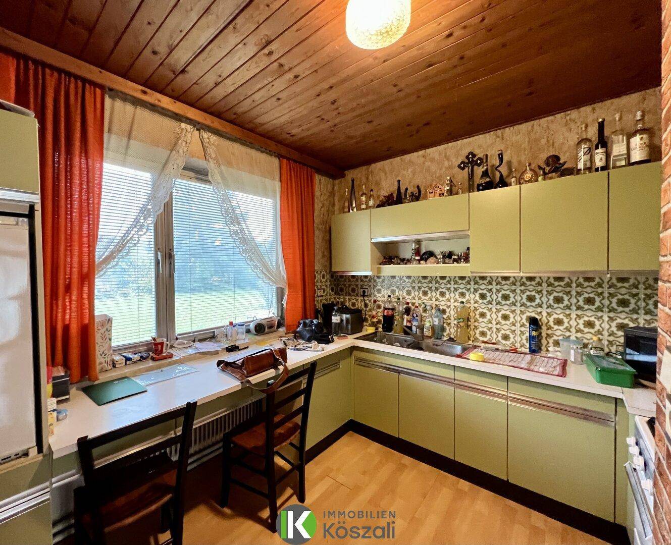 Küche im Retro-Stil mit grünen Schränken, Holzdecke und großem Fenster mit Blick ins Grüne.