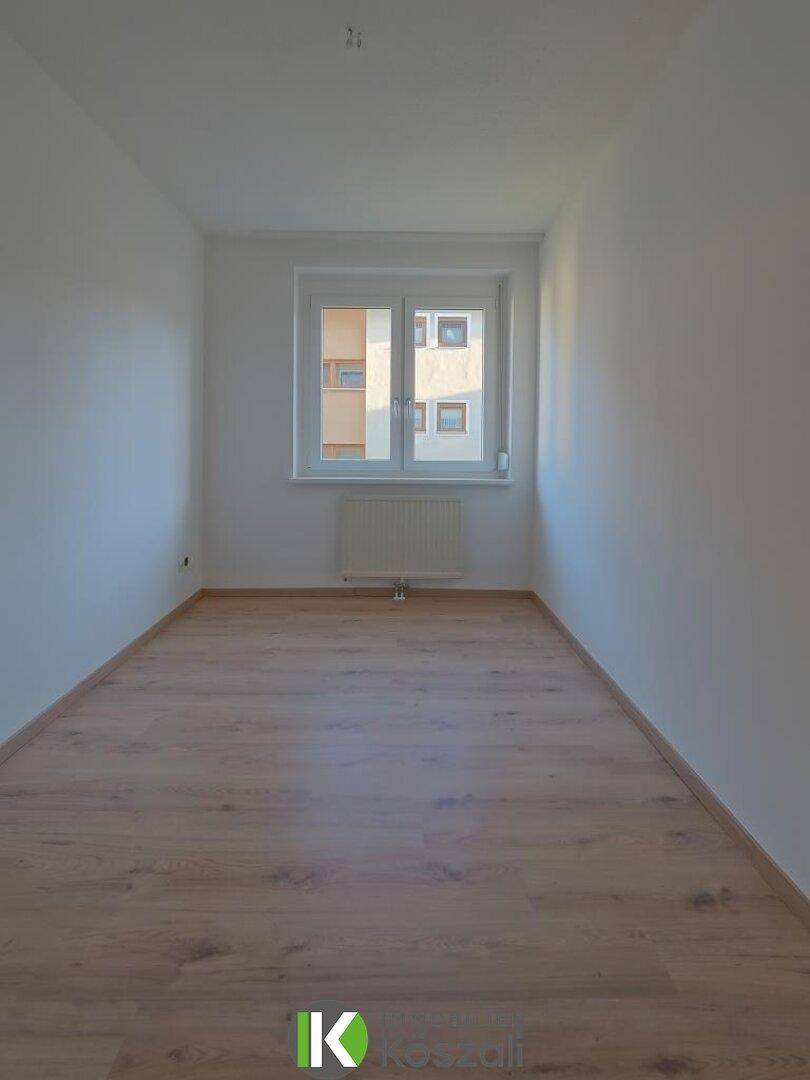 Freundliches, leeres Zimmer mit Holzboden und Fenster, bietet vielseitige Nutzungsmöglichkeiten.