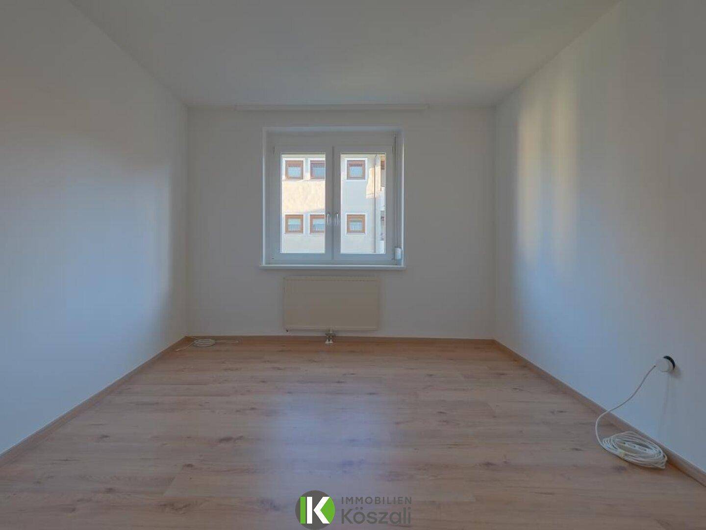 Helles, leeres Zimmer mit Holzboden und Fenster, ideal als Schlaf- oder Arbeitszimmer nutzbar.