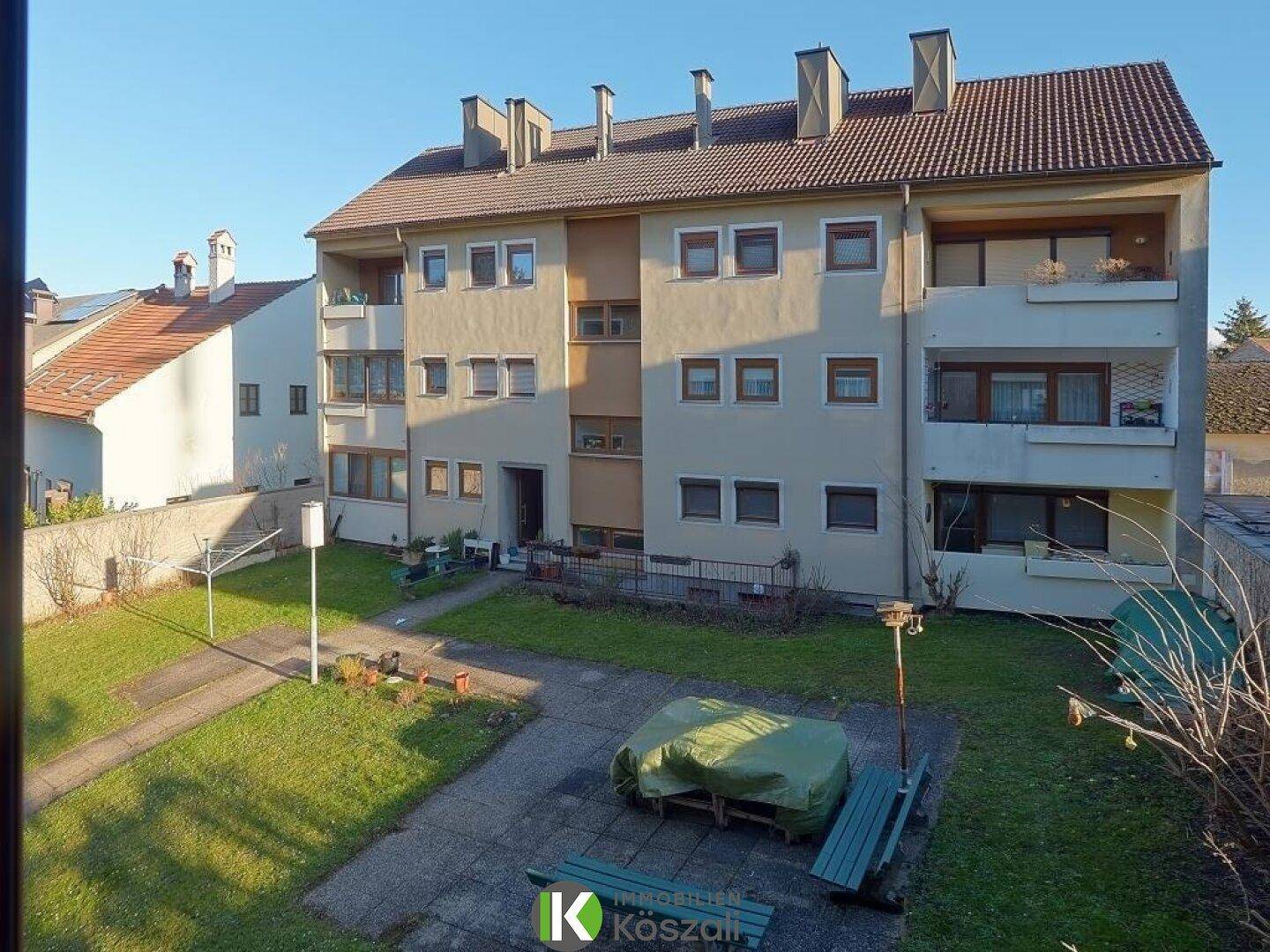 Mehrfamilienhaus mit gepflegtem Gemeinschaftsgarten und Sitzgelegenheiten im Freien.