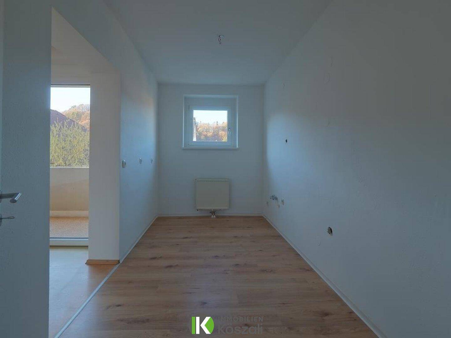 Helles Zimmer mit Holzboden und Fenster, mit offenem Zugang zu einem weiteren Raum mit Balkon.