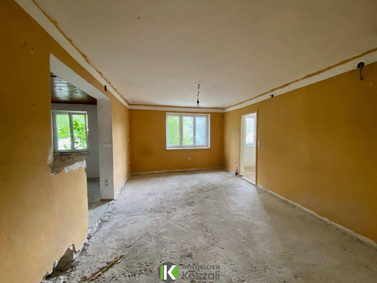 Geräumiger Wohnbereich in Renovierung mit gelben Wänden und Betonboden, bereit für den Ausbau.