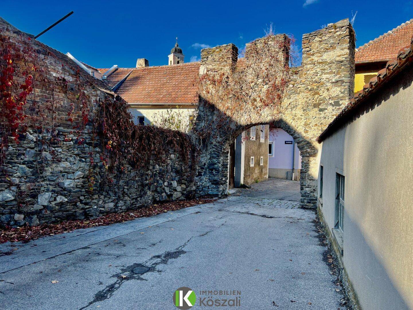 Historische Gasse mit alten Steinmauern und einem Torbogen, der zu weiteren Gebäuden führt.