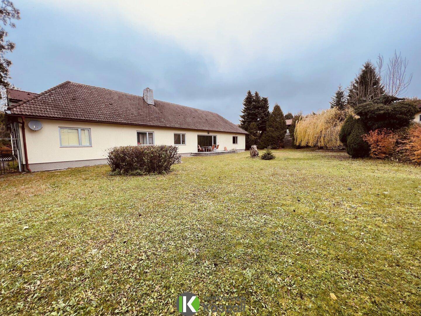 Weitläufiger Garten mit Rasenfläche und Blick auf die Rückseite des Hauses und die umliegende Natur.