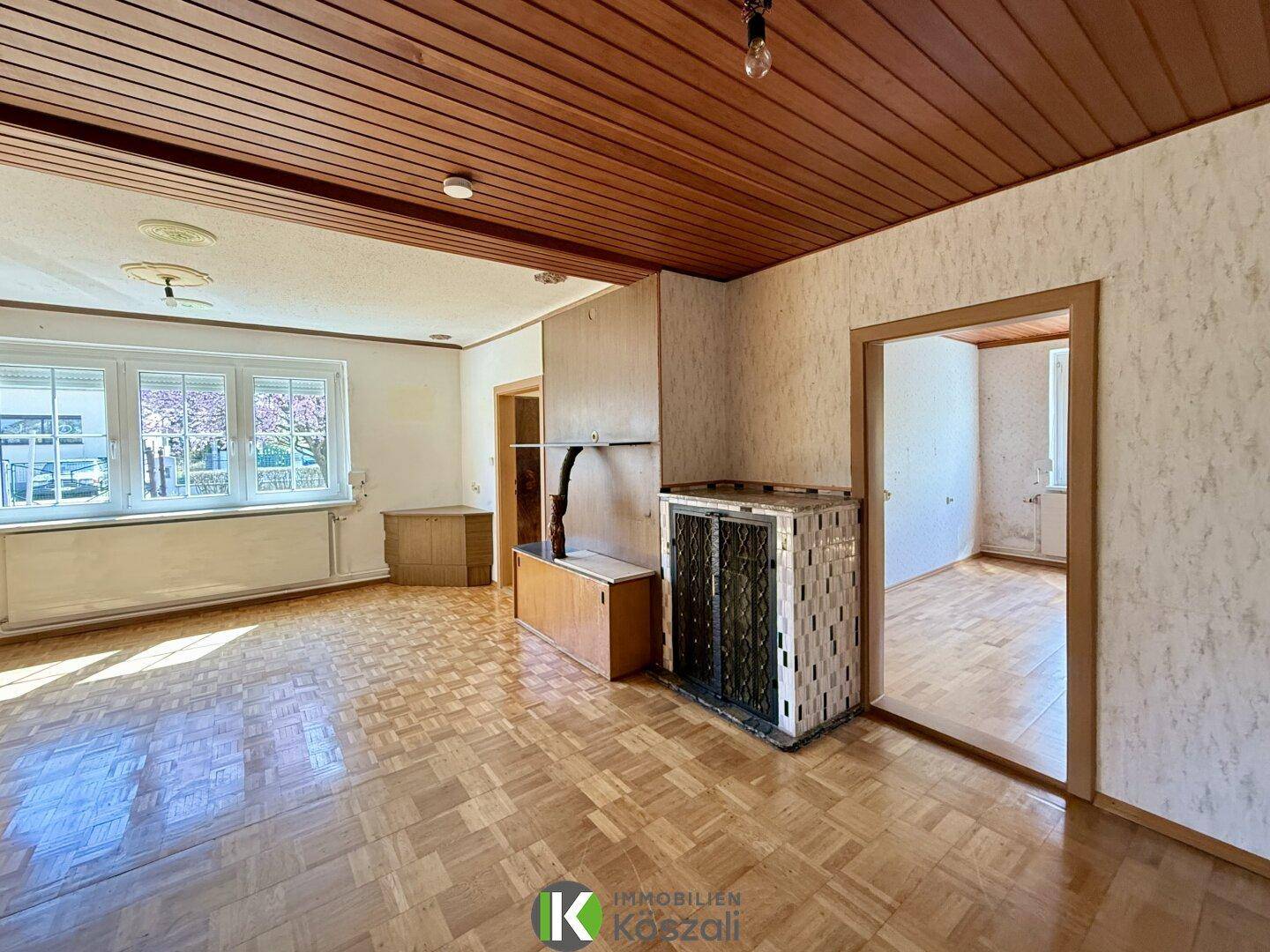 Geräumiges Wohnzimmer mit Parkettboden, Holzdecke und traditionellem Kachelofen.