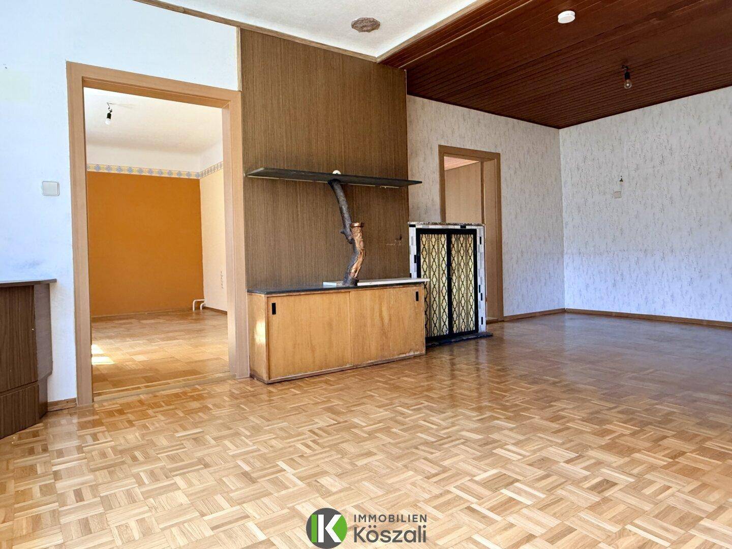 Großes Wohnzimmer mit Parkettboden, Holzdecke und einem dekorativen Kachelofen.