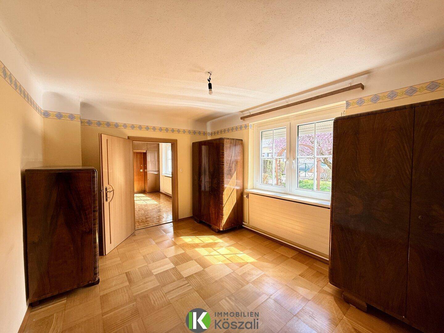 Sonniges Schlafzimmer mit Parkettboden und klassischen Holzschränken, mit Blick ins Grüne.