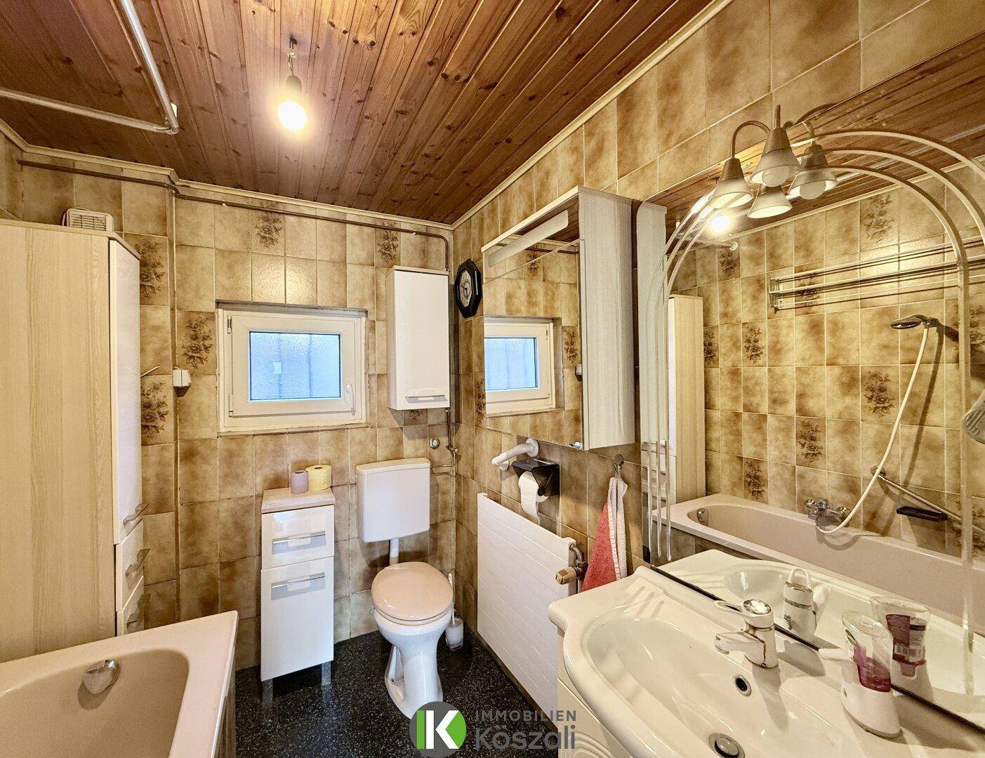 Badezimmer im 80er-Jahre-Stil mit braunen Fliesen, Holzdecke, Badewanne und WC.