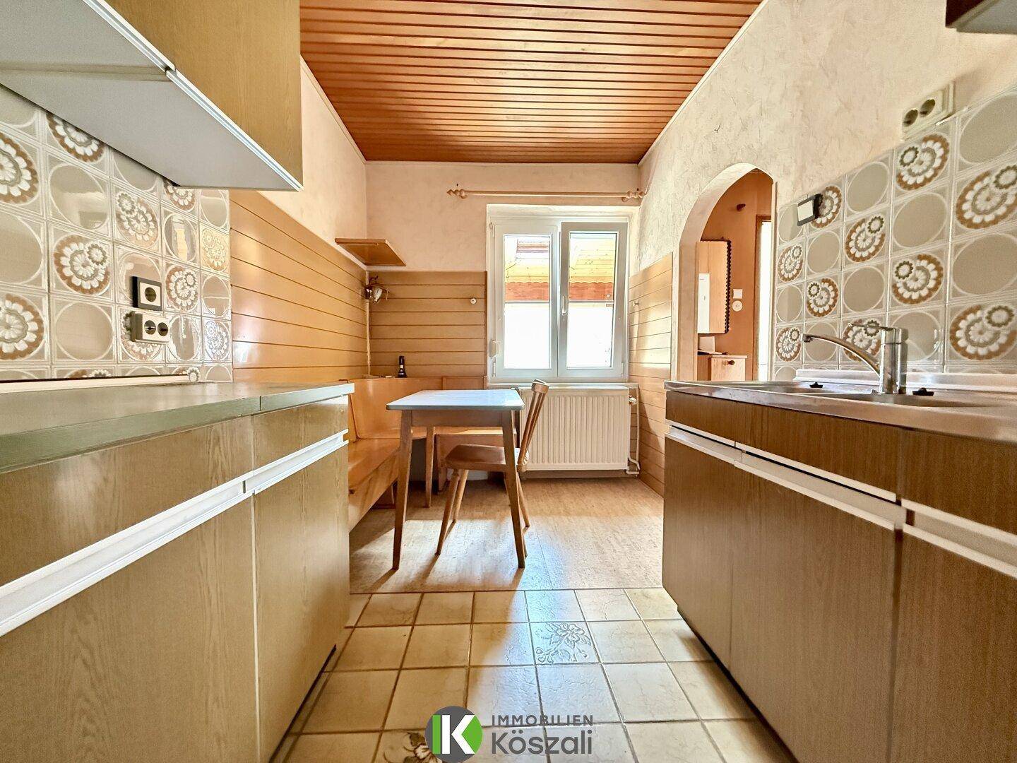 Traditionelle Küche mit Fliesenboden, Holzdecke und integrierter Essecke am Fenster.